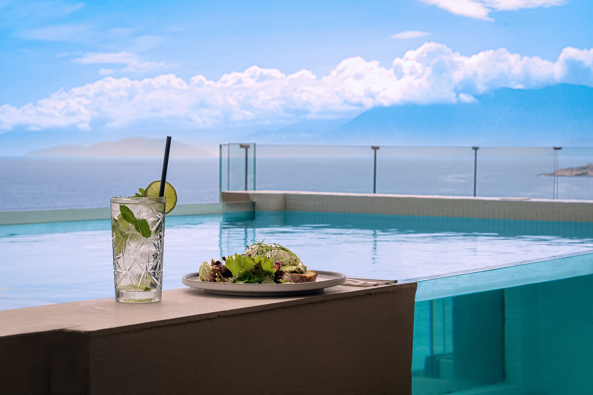 a table with a glass of water and a glass with a lemon on it by a beach