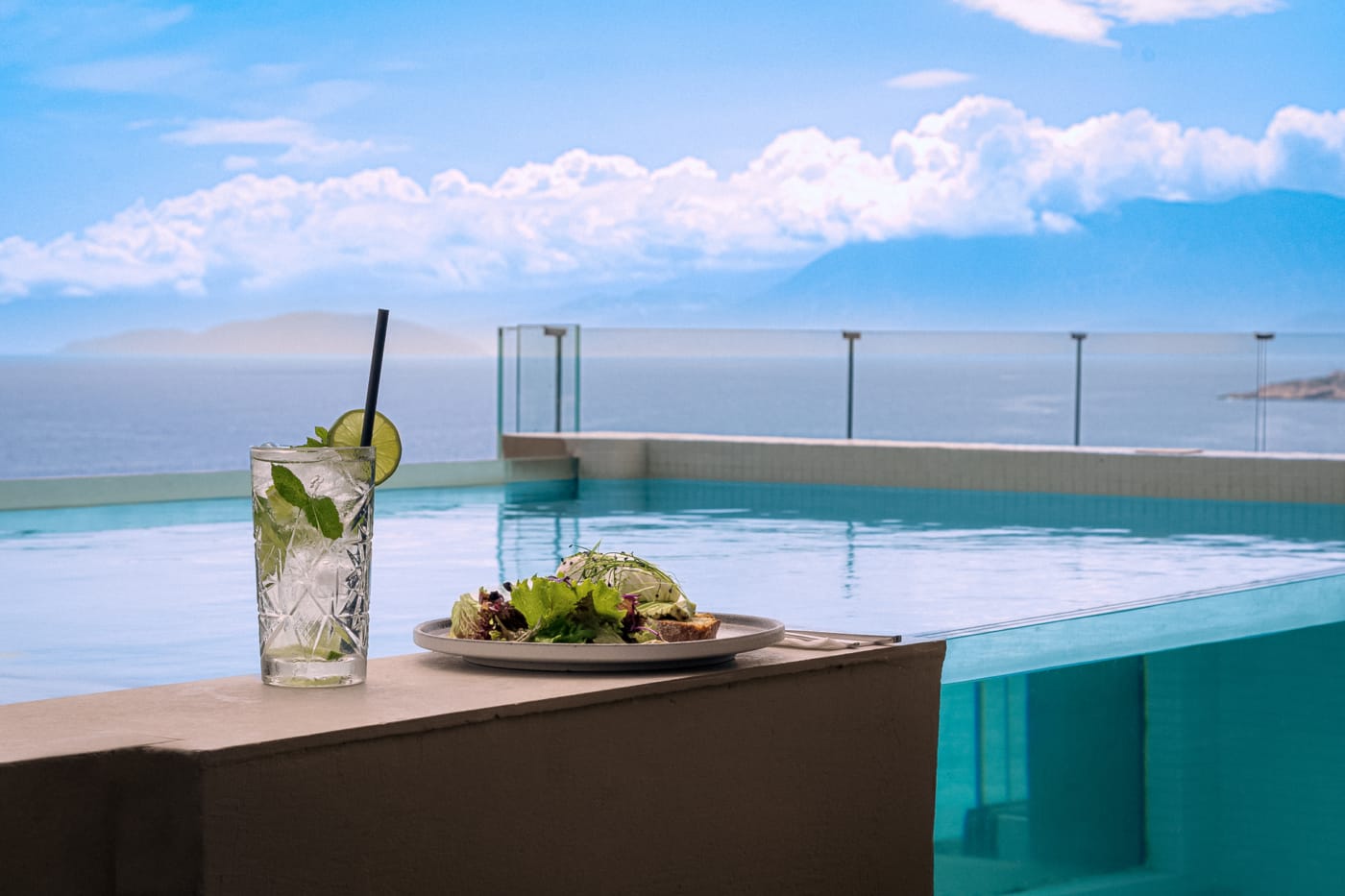 a table with a glass of water and a glass with a lemon on it by a beach