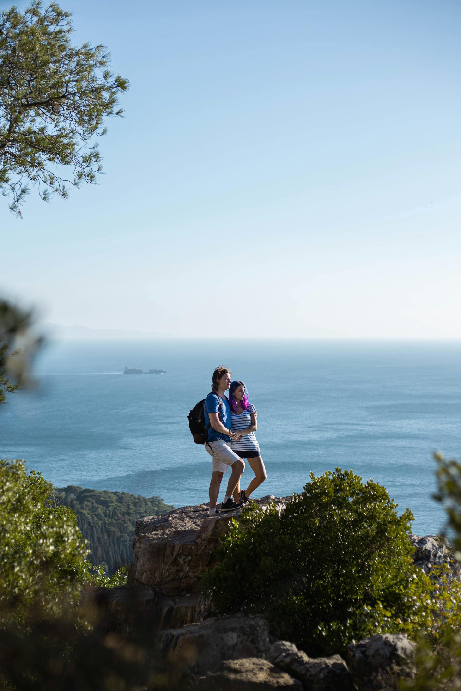 a man and woman posing on a rock overlooking a body of water
