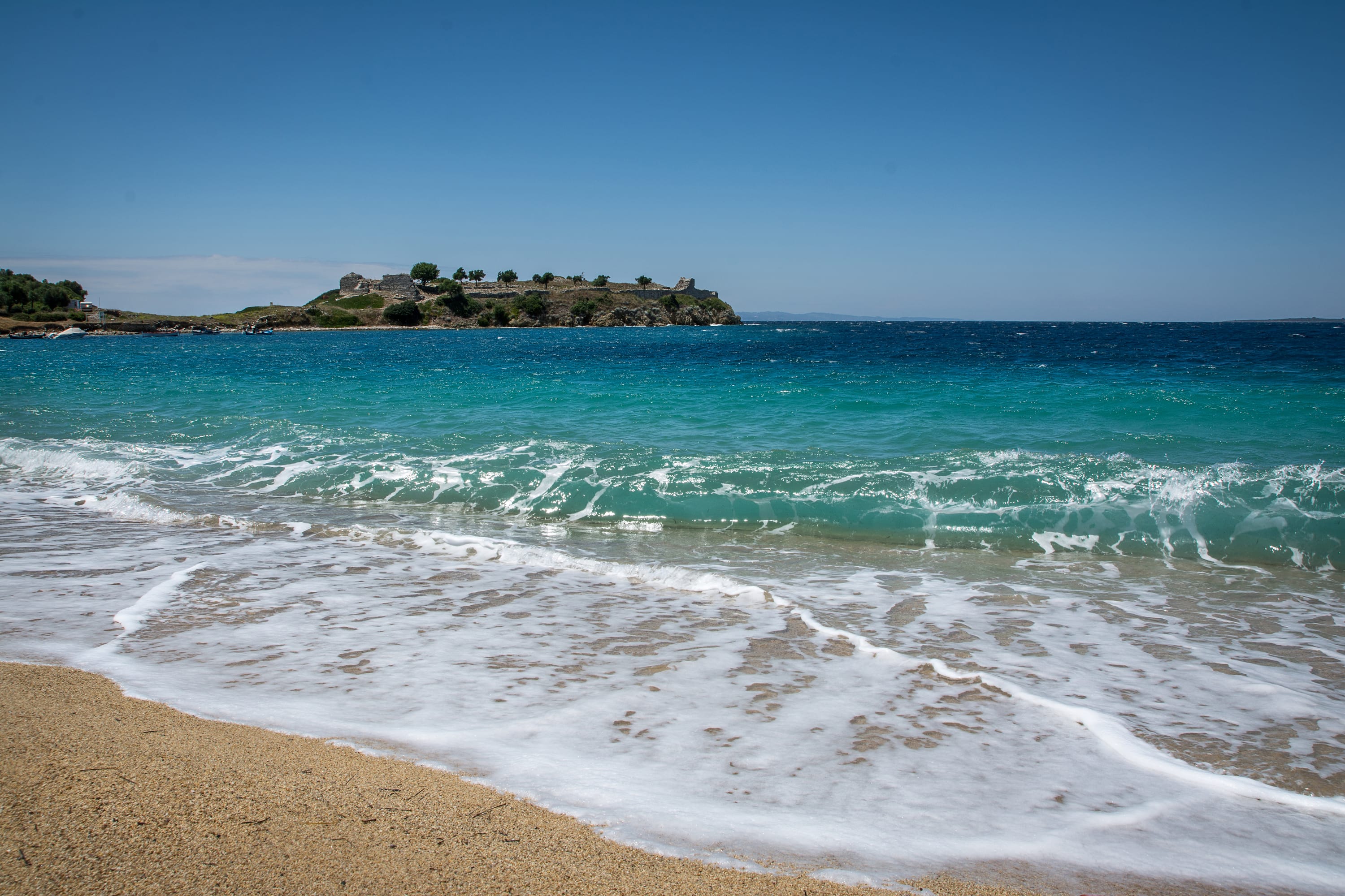 a beach with waves and a small island in the distance