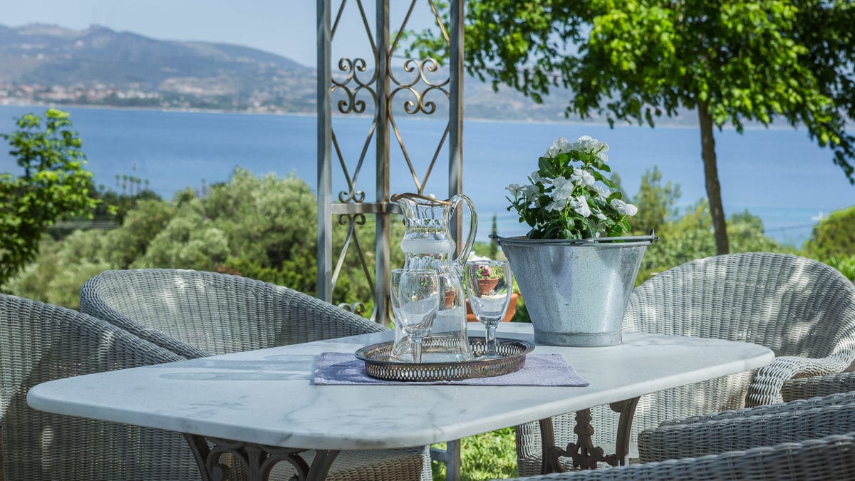 a table with glasses and a vase on it by a body of water