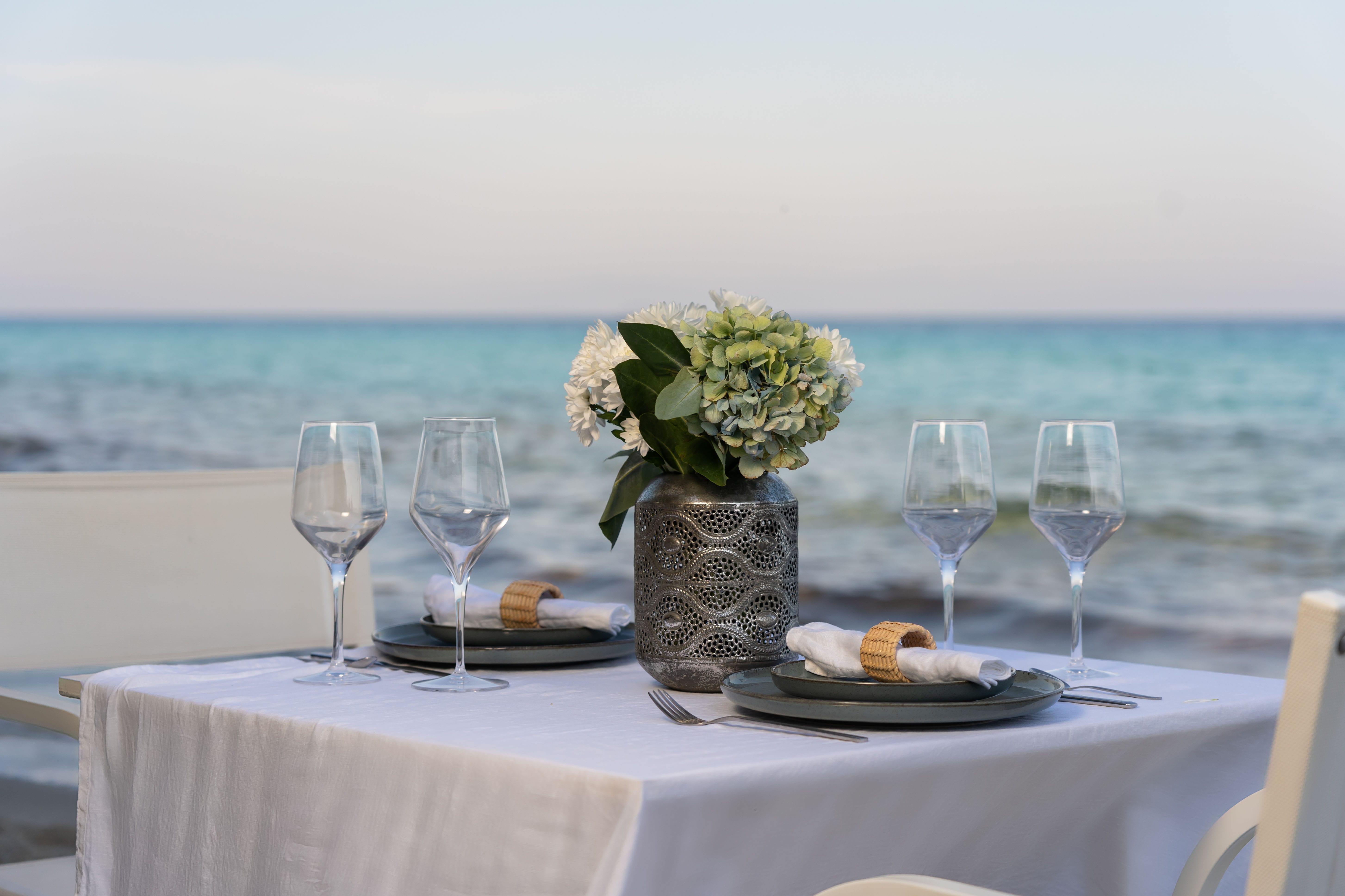 a table with glasses and plates of food on it by a body of water