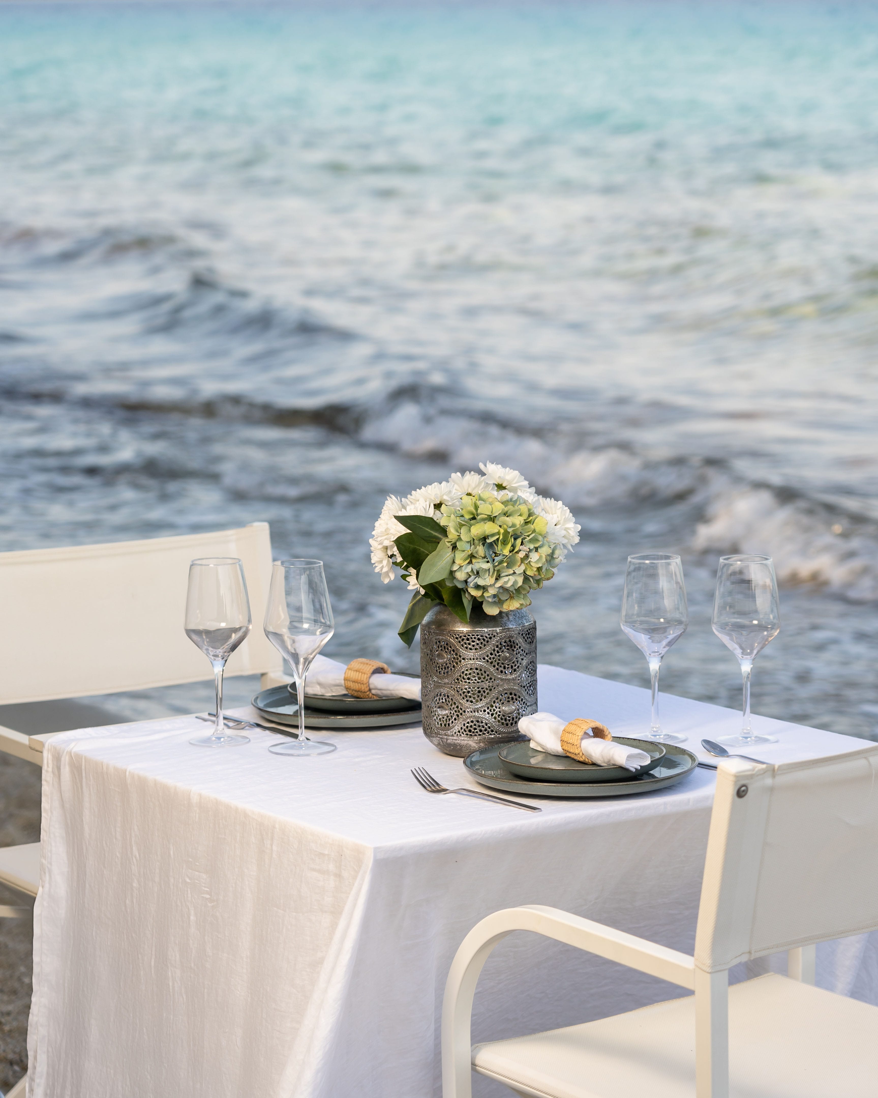 a table with glasses and plates on it by a body of water