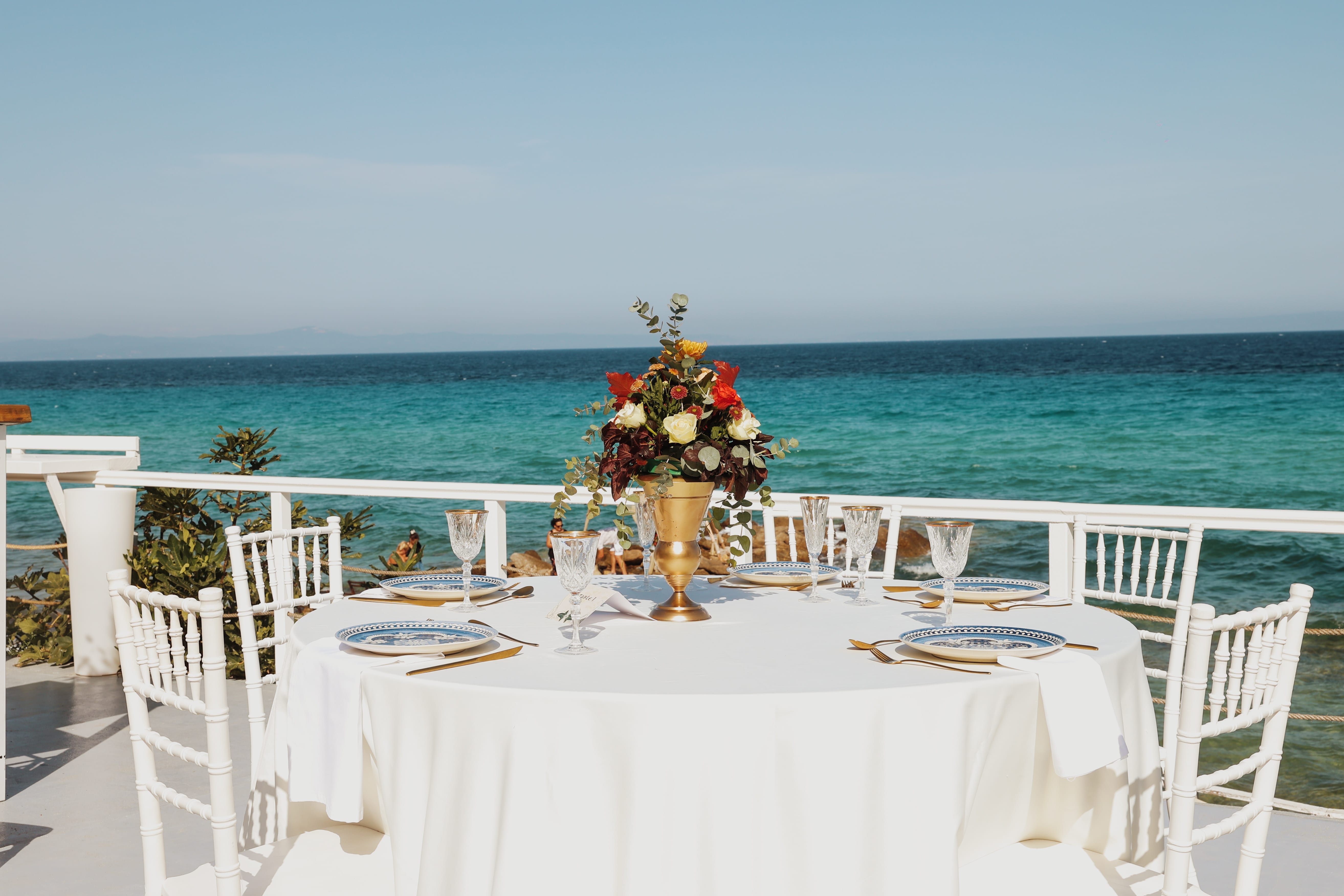 a table with a vase of flowers on it by a beach