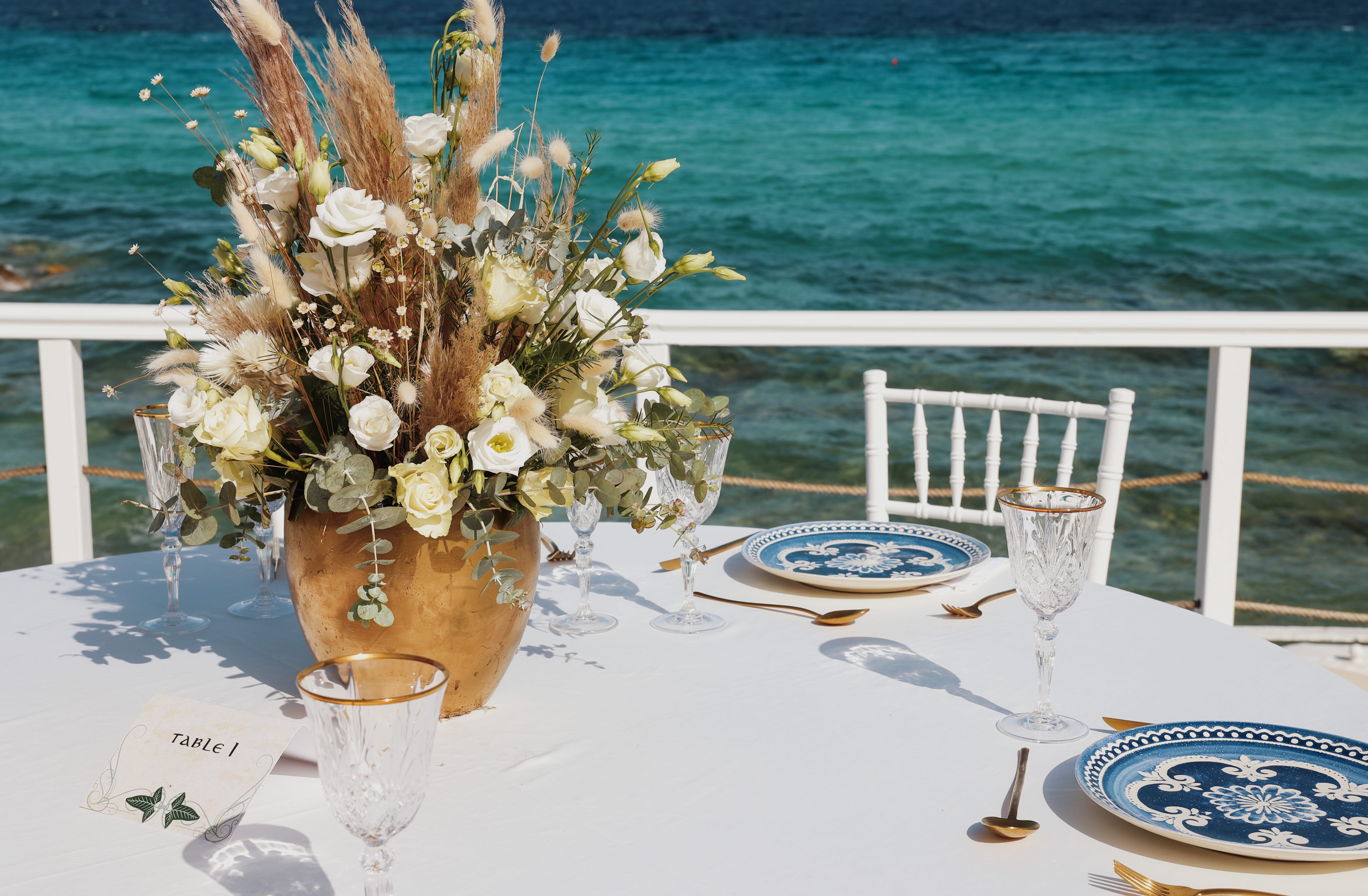 a vase with white flowers on a table by a body of water