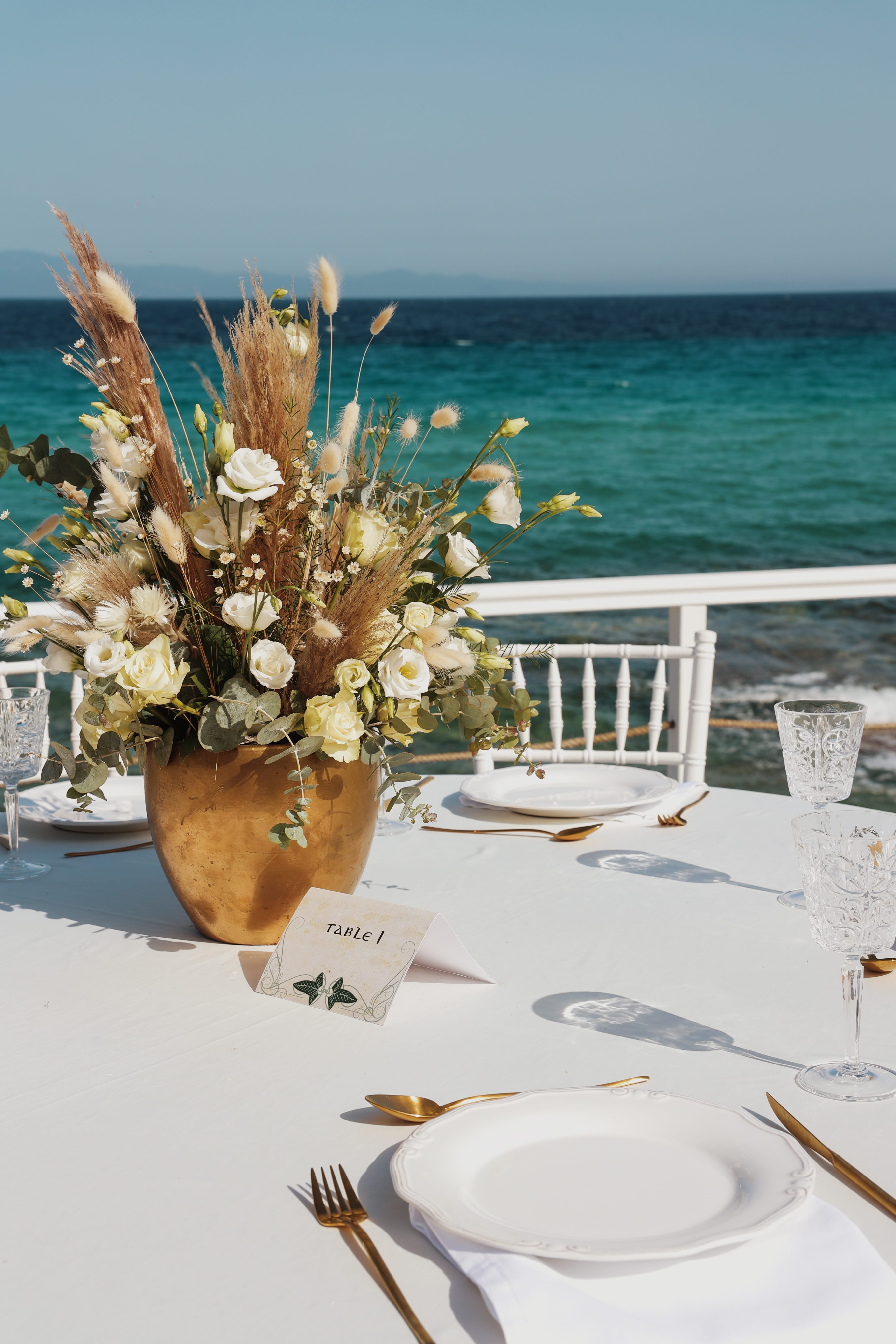 a vase with white flowers on a table by a beach