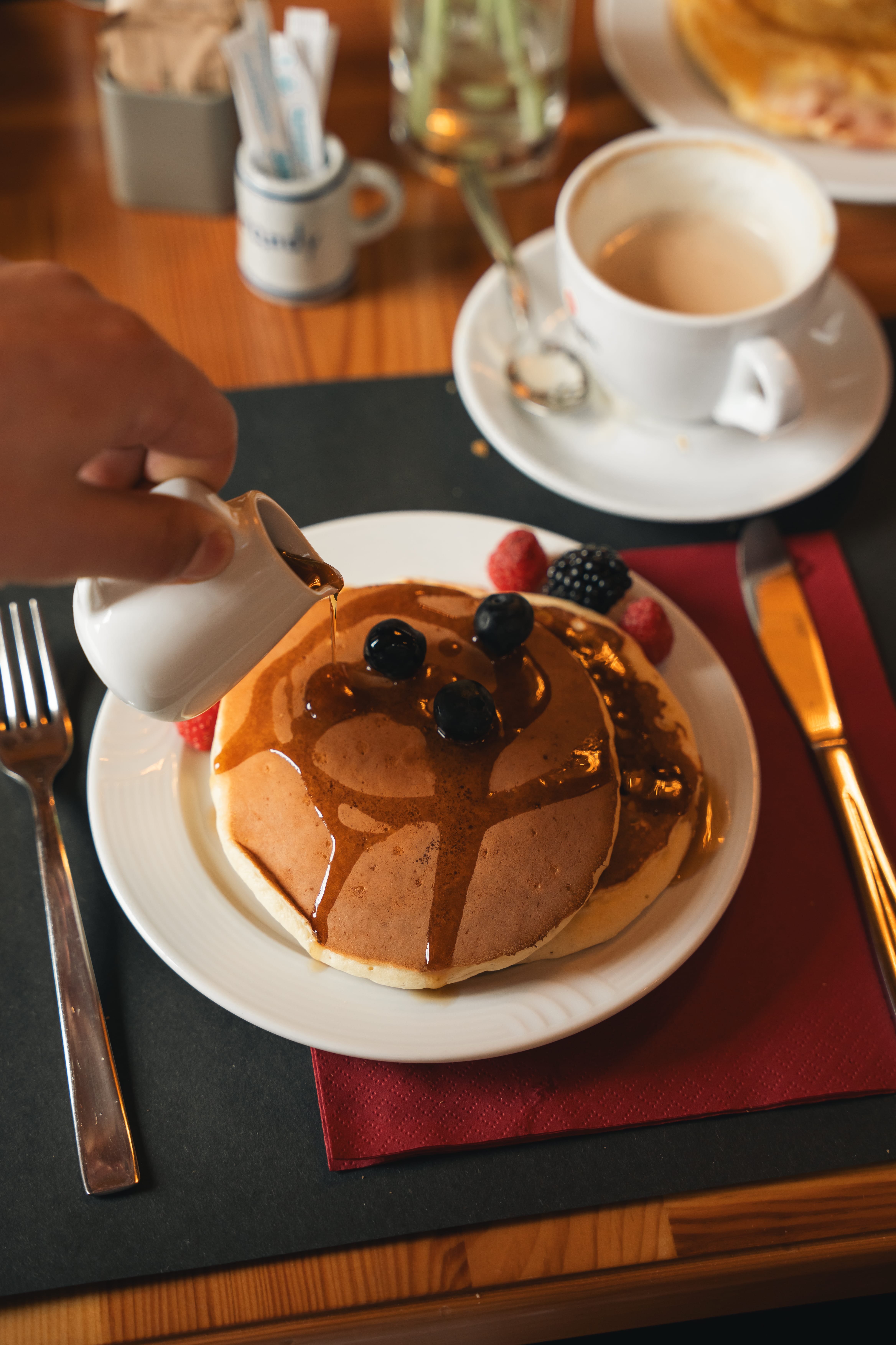 a person pouring syrup onto pancakes