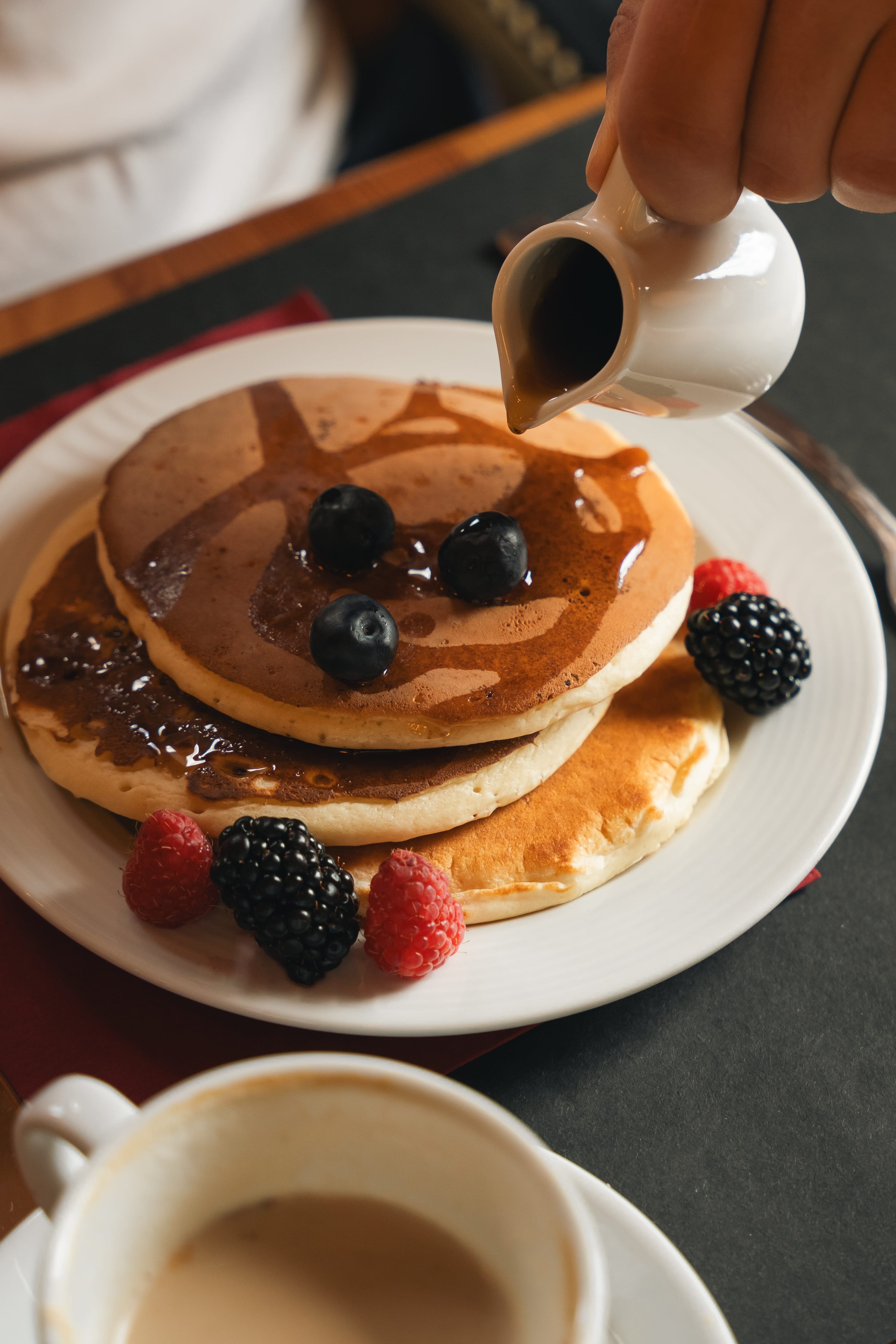 a person pouring syrup on a stack of pancakes