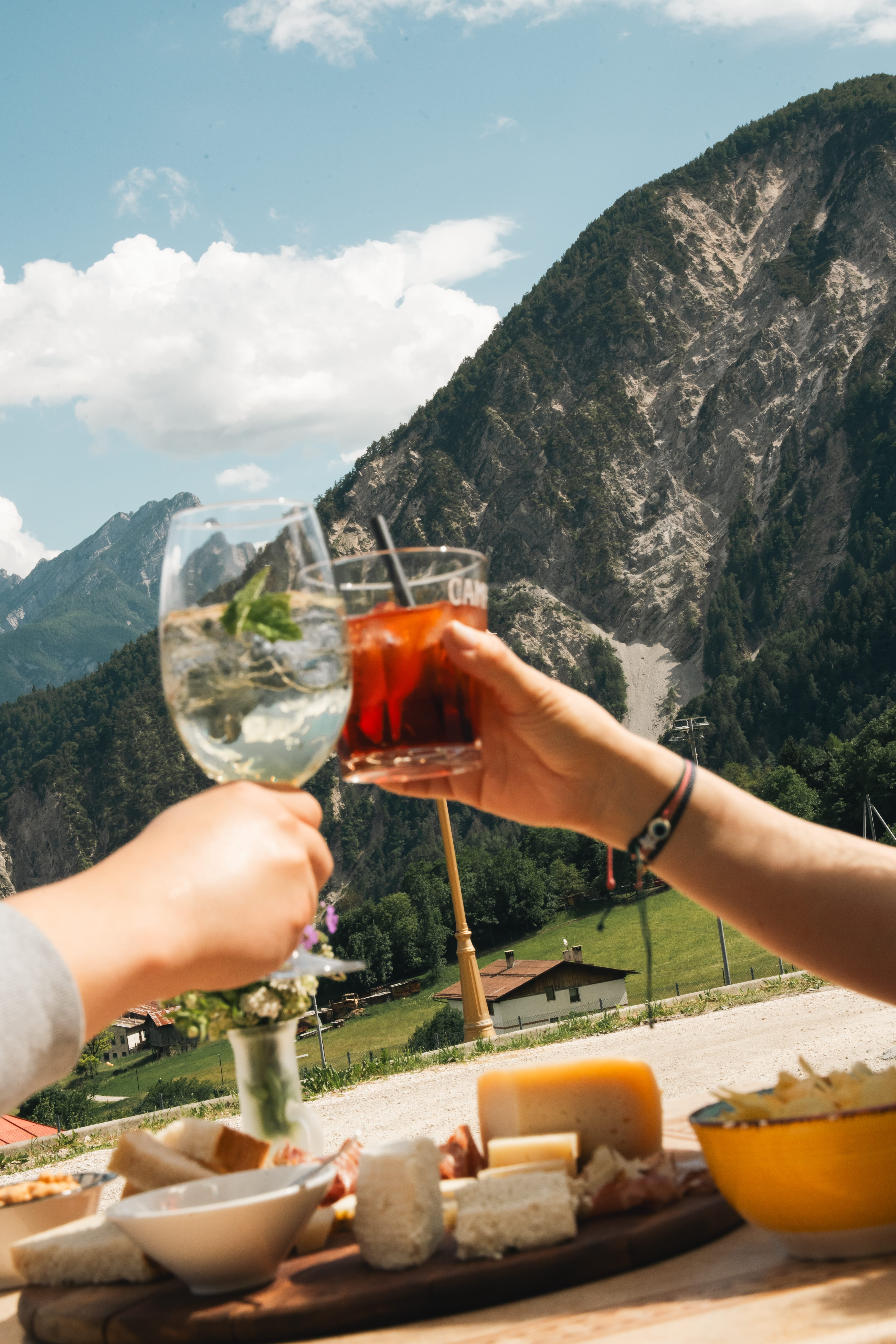 a couple of hands holding wine glasses with a mountain in the background