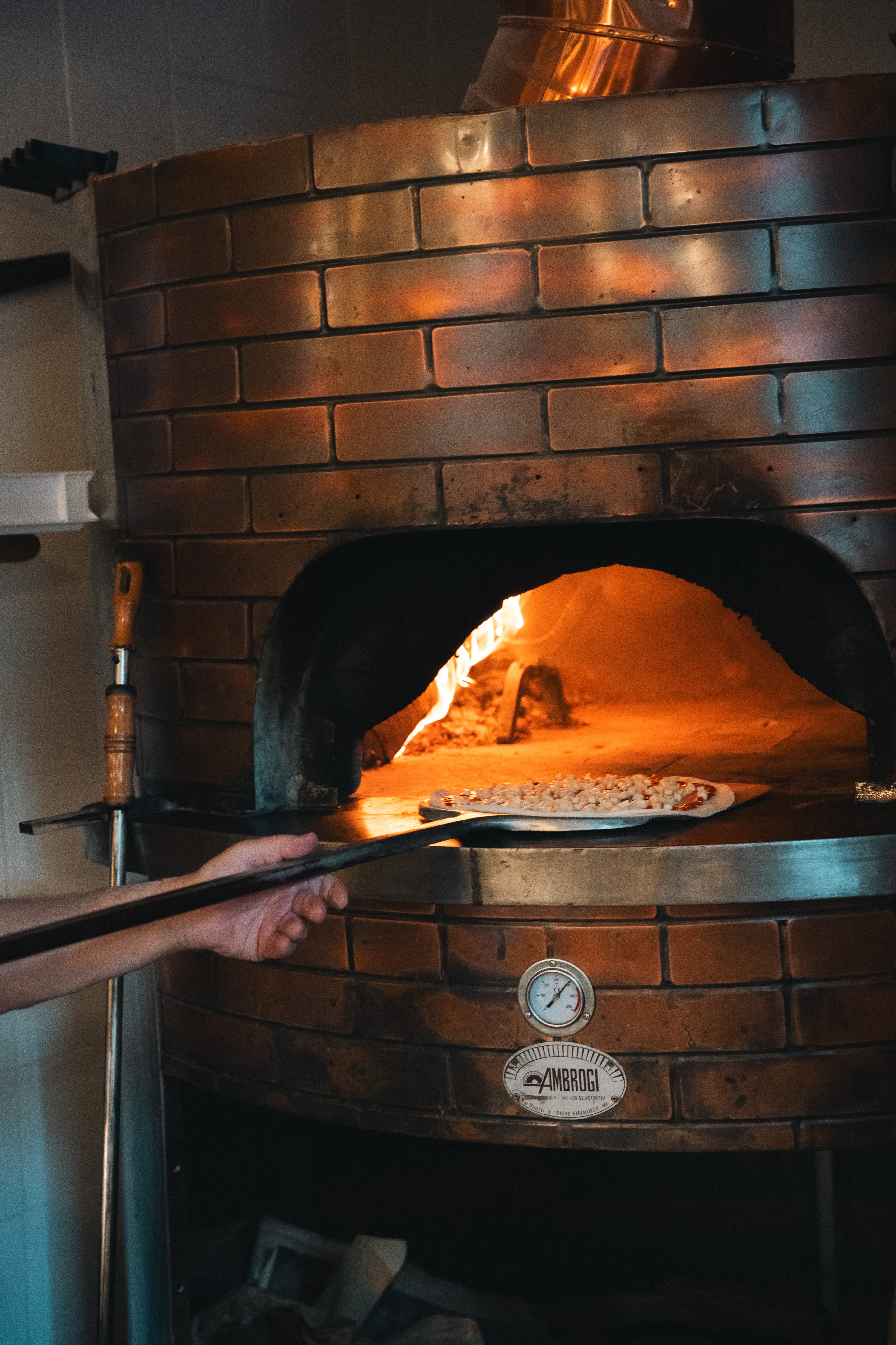a hand holding a pizza in a brick oven
