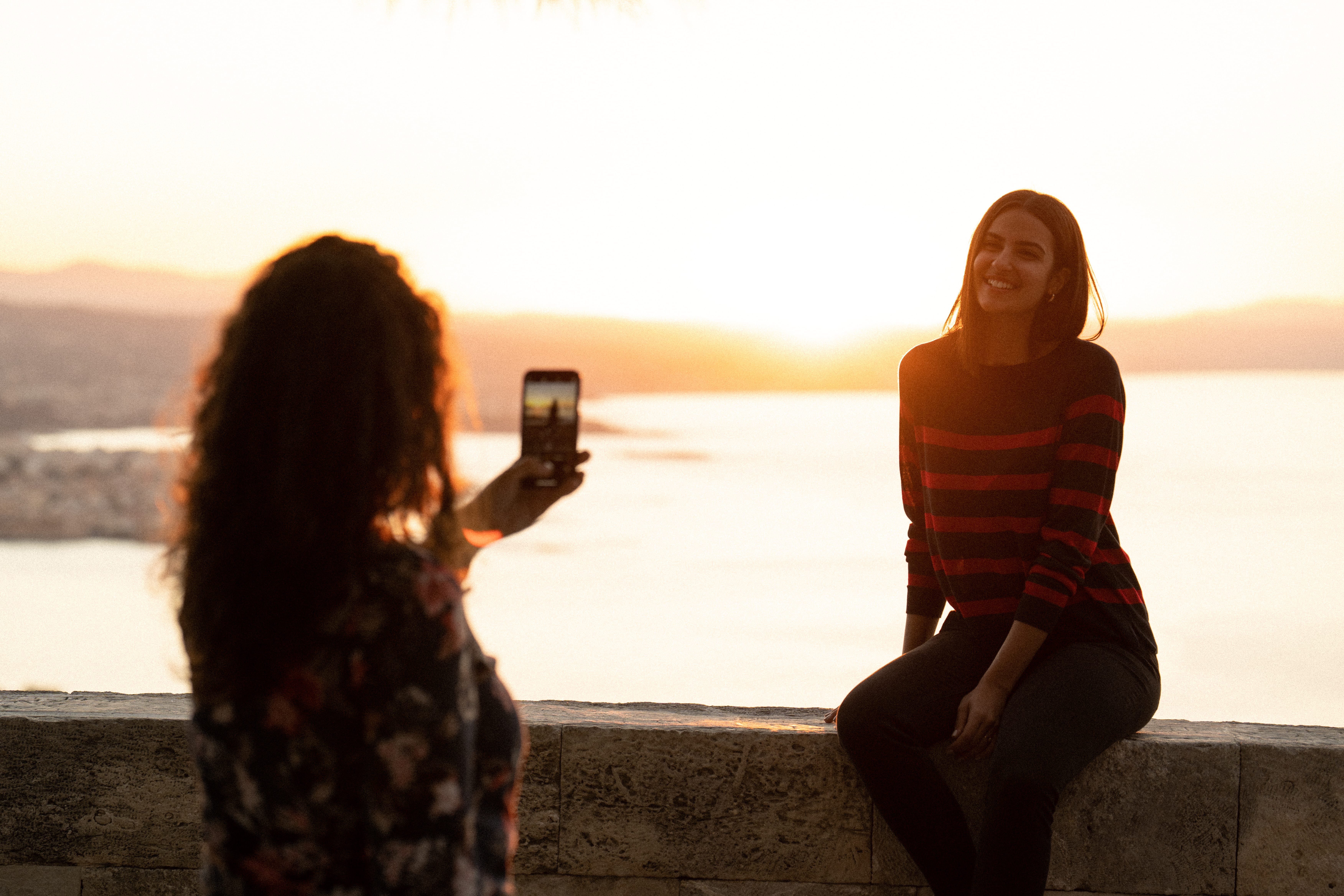 a couple of women sitting on a ledge looking at a cell phone