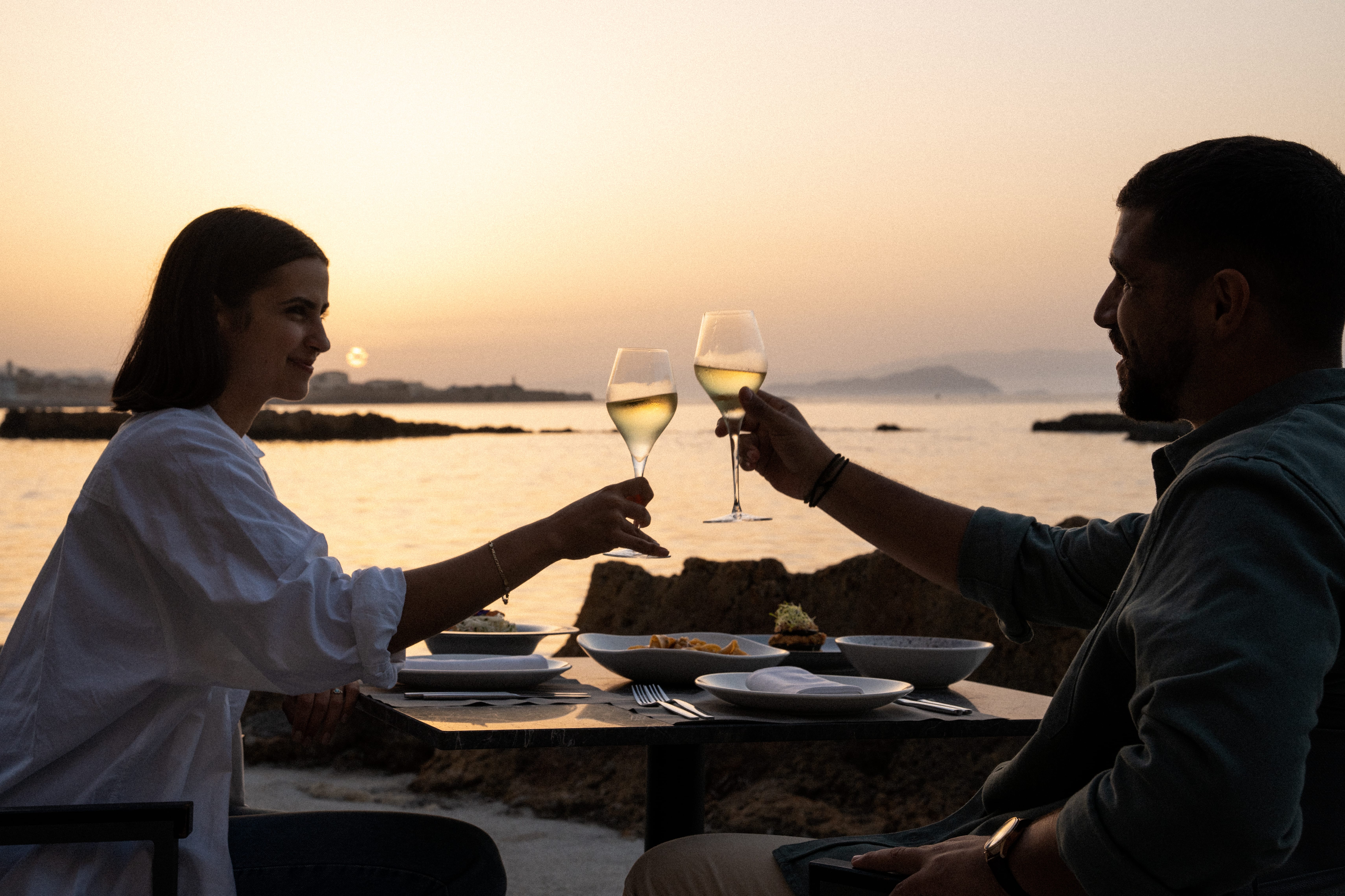 a man and woman sitting at a table with food and drinks