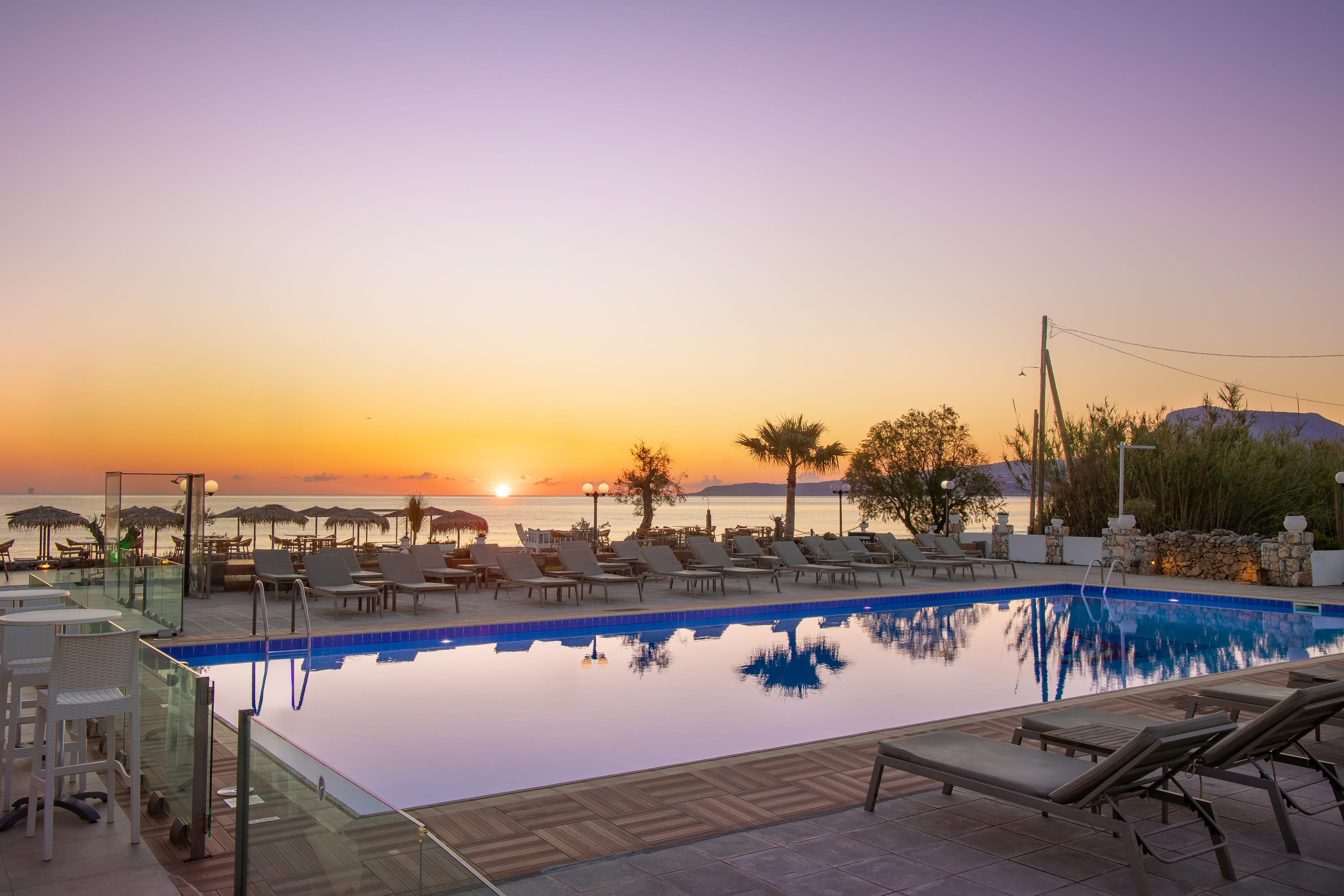 a pool with chairs and a sunset