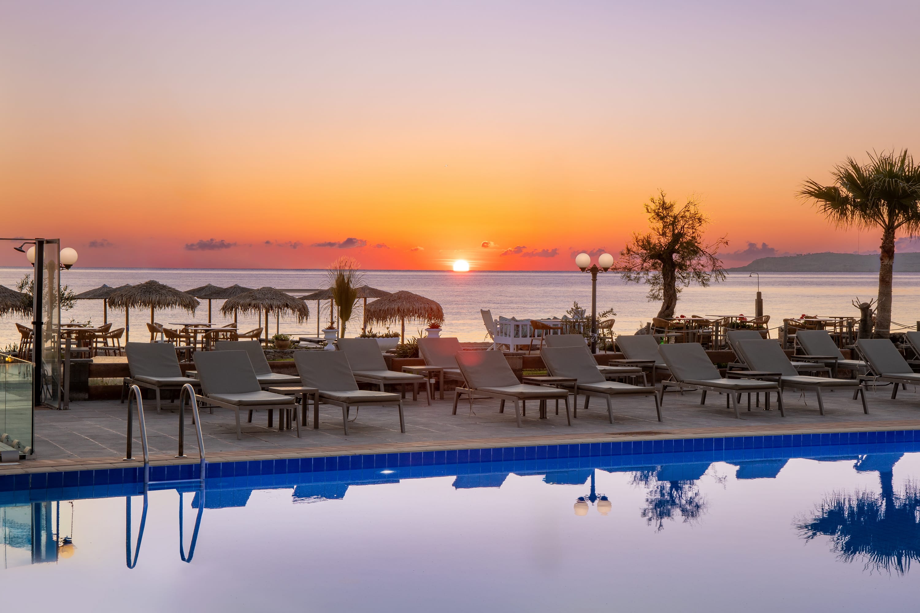 a pool with chairs and umbrellas in front of a sunset