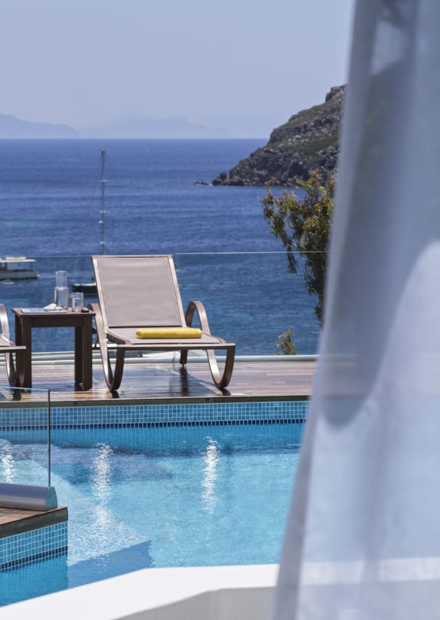 a pool with chairs and a table by a window with a view of the ocean