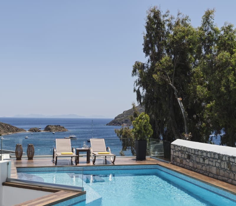 a pool with chairs and a table by it by a beach