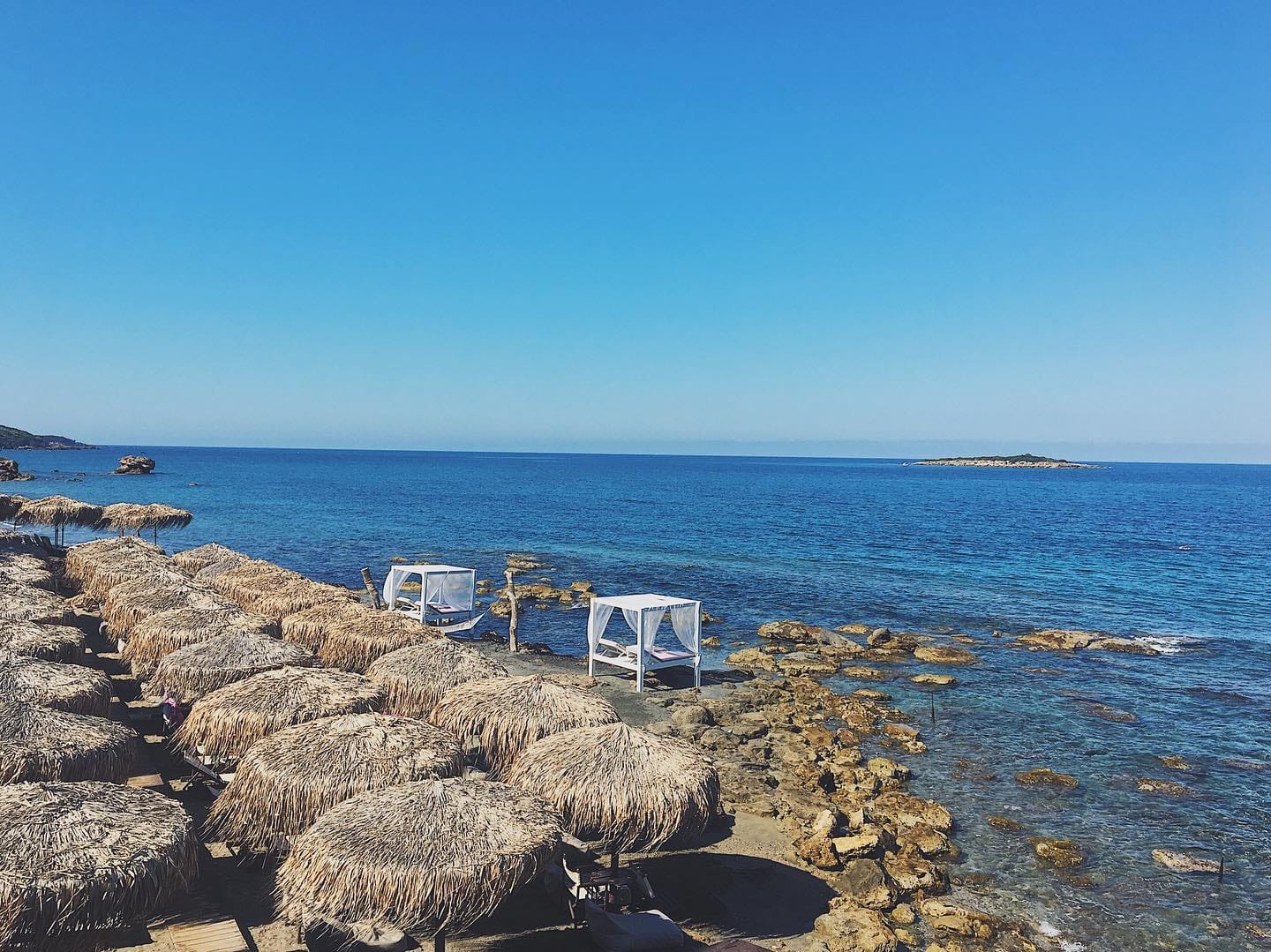 a beach with straw umbrellas and a group of chairs on the shore
