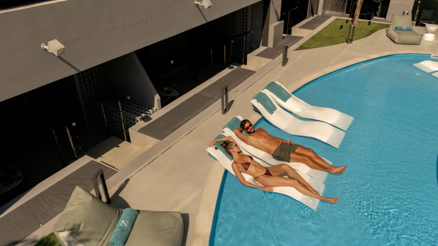 a person and person lying on lounge chairs near a pool