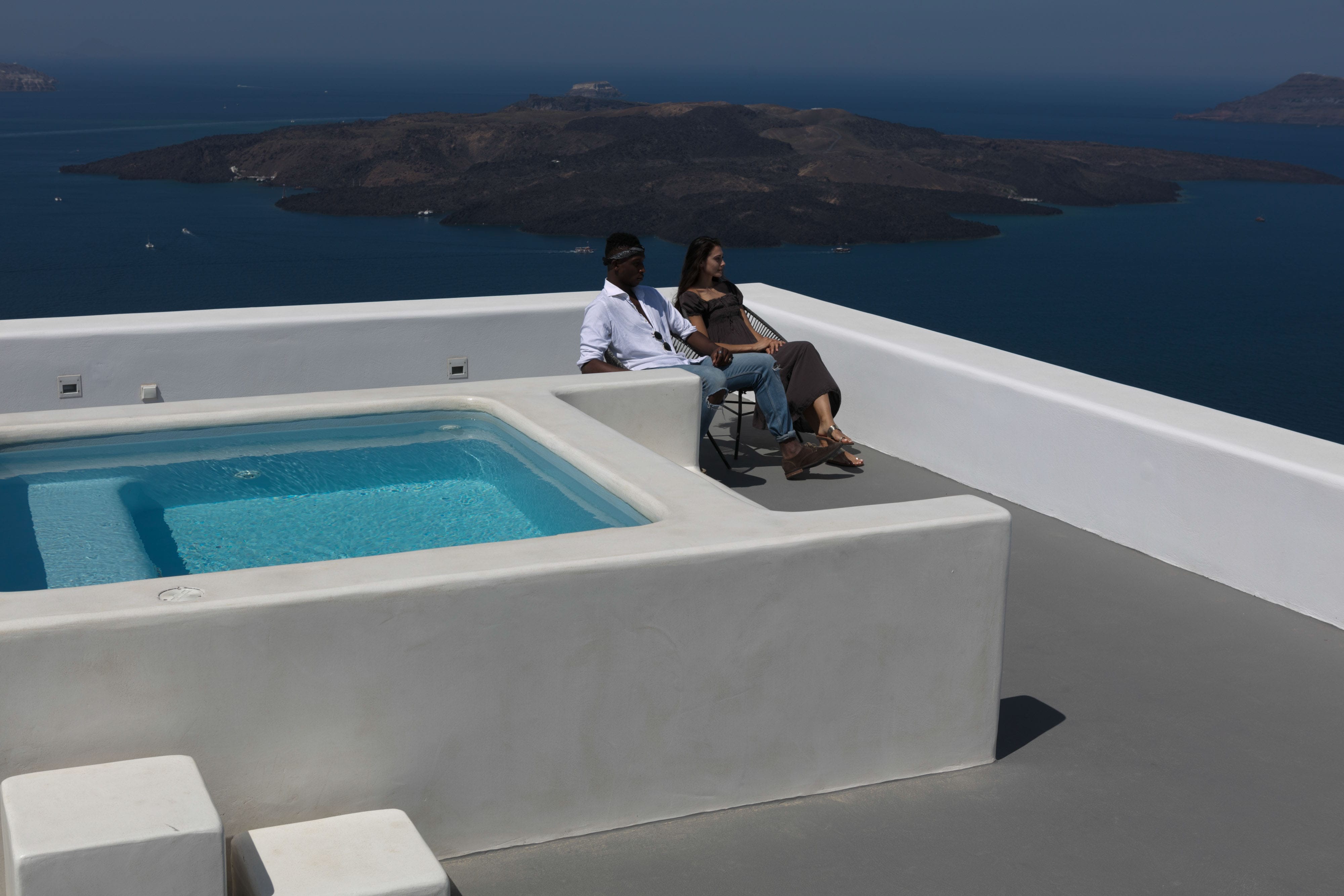 a person and person sitting on a rooftop overlooking a pool