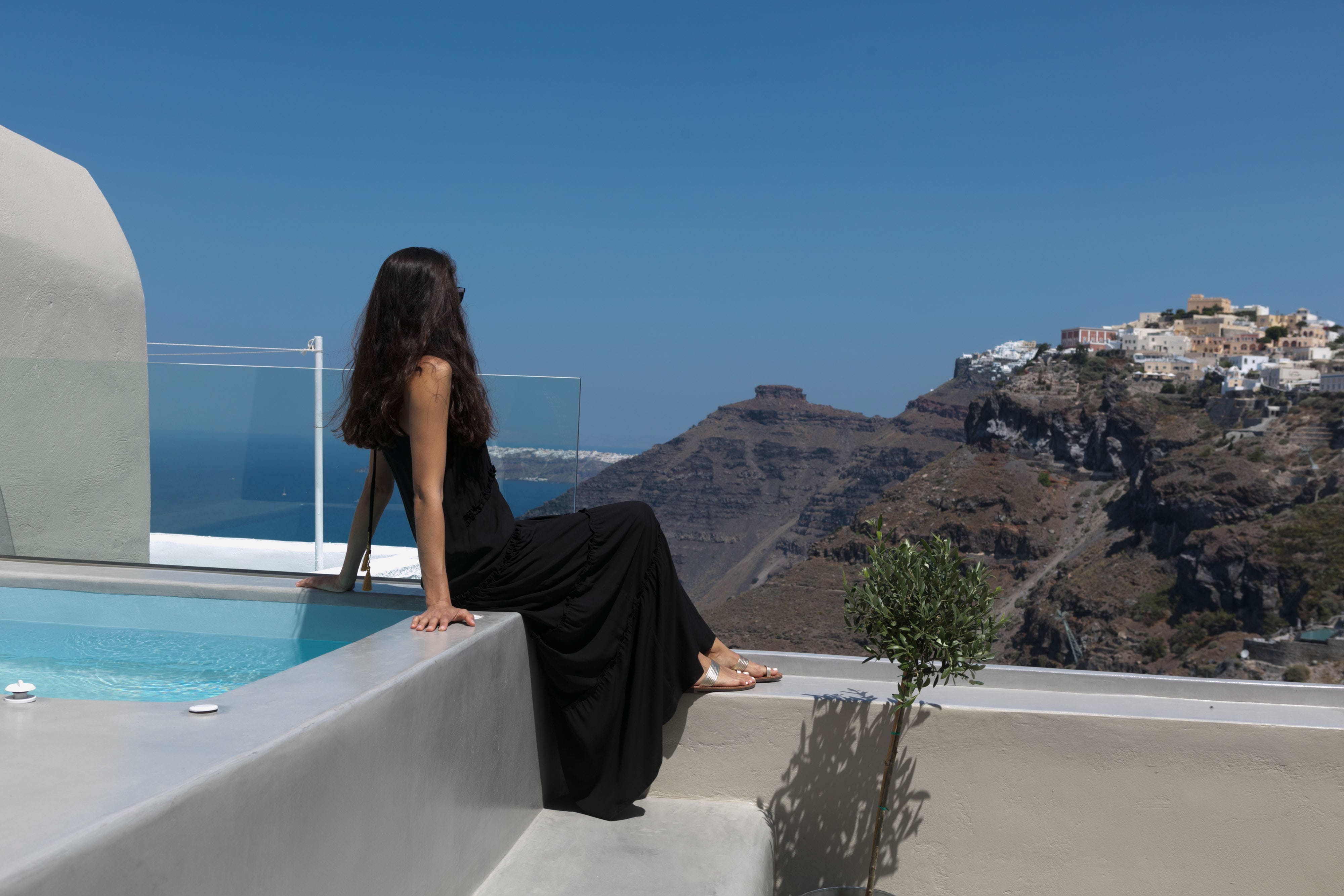 a person in a black dress sitting on a ledge overlooking a pool
