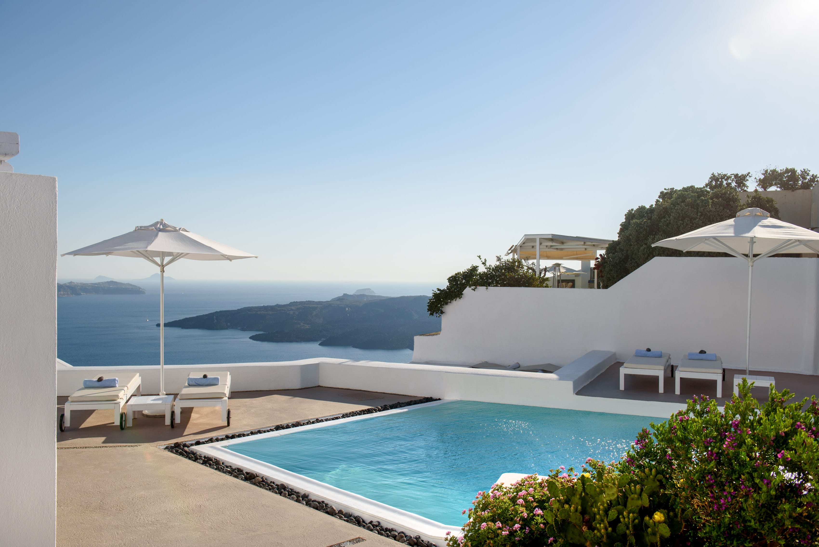 a pool with a white wall and a white building with a view of the ocean