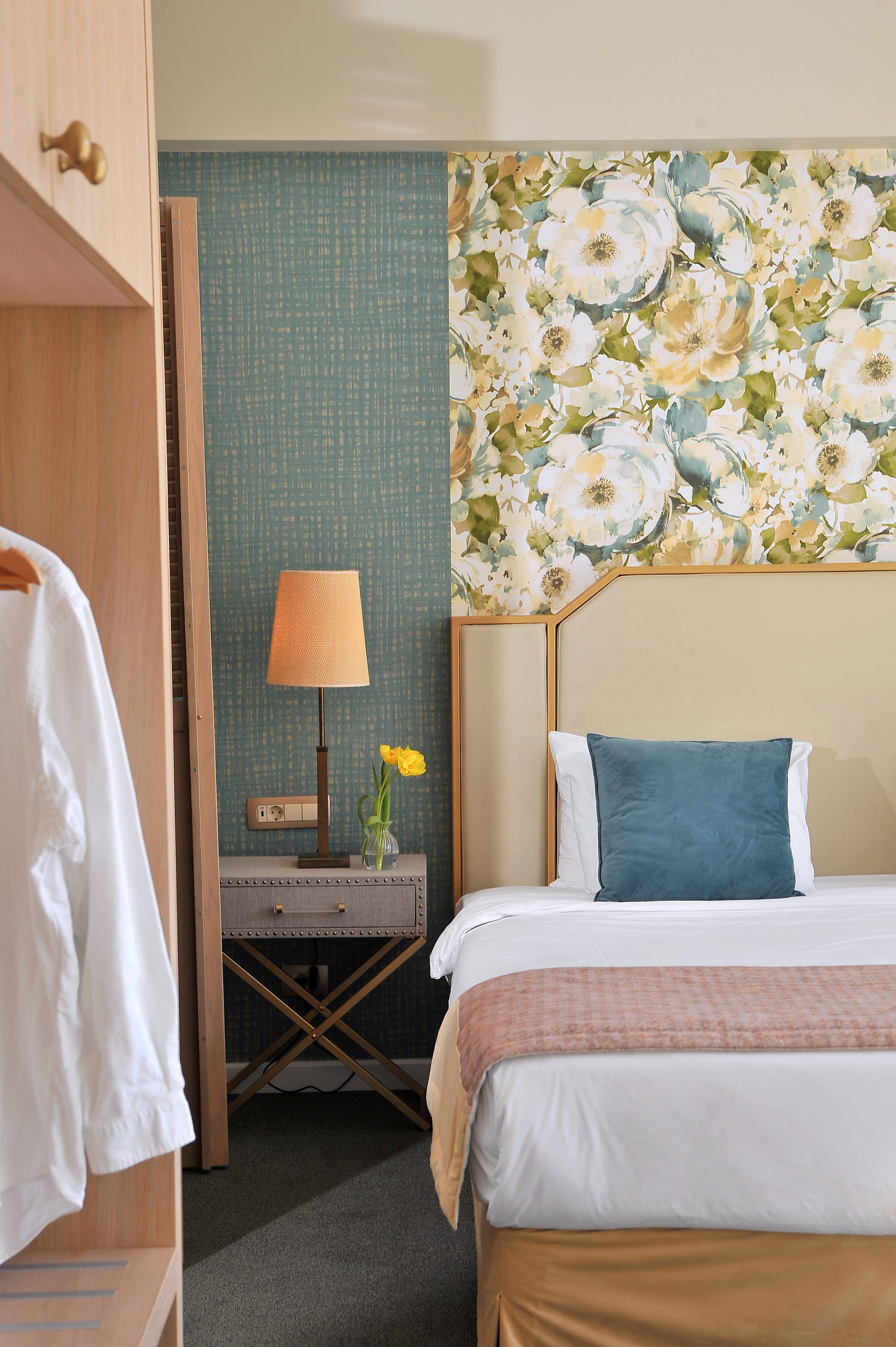 a bed with a lamp and a table with flowers on the wall