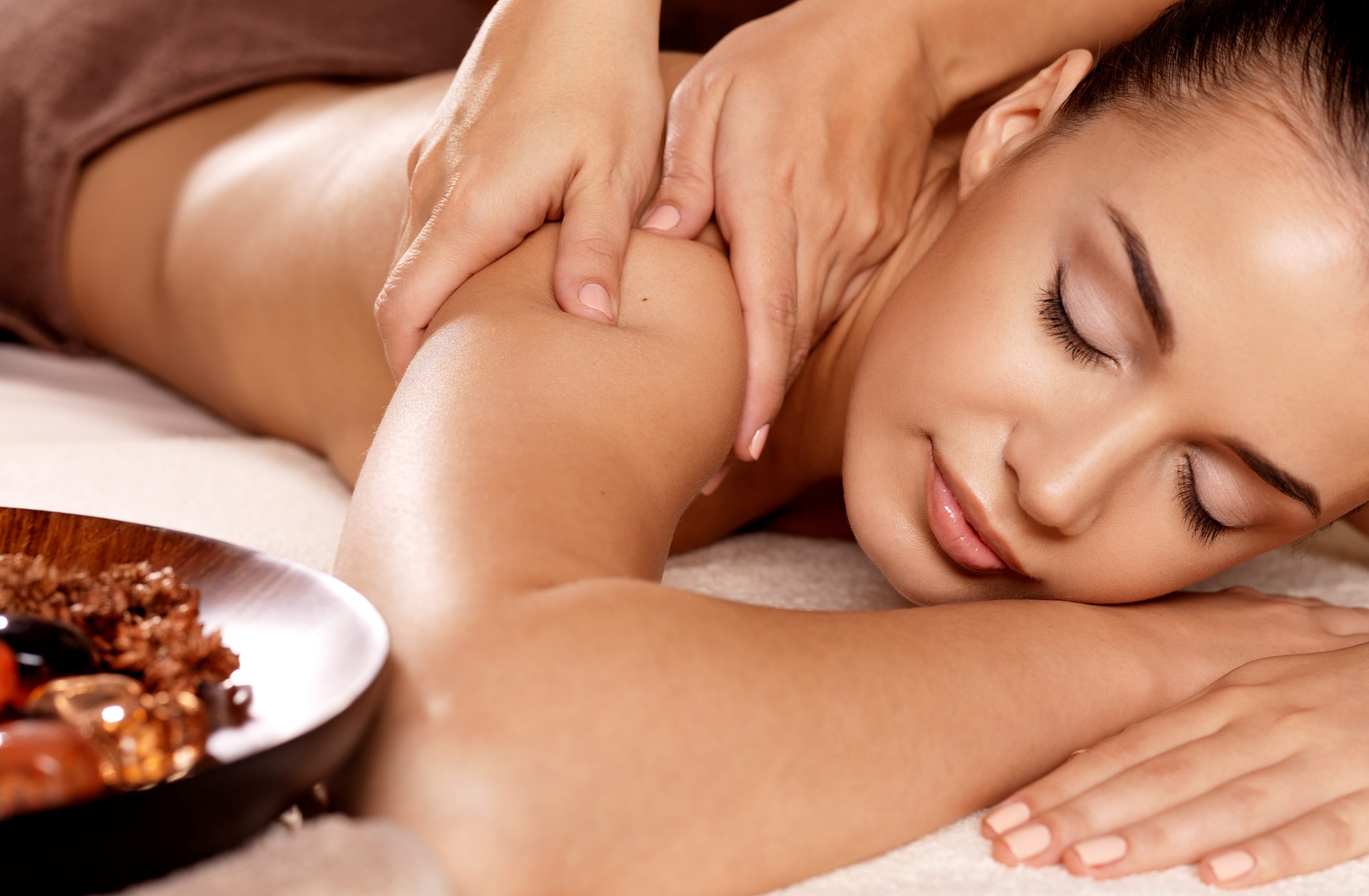 a person lying down on a bed with hands on her shoulder