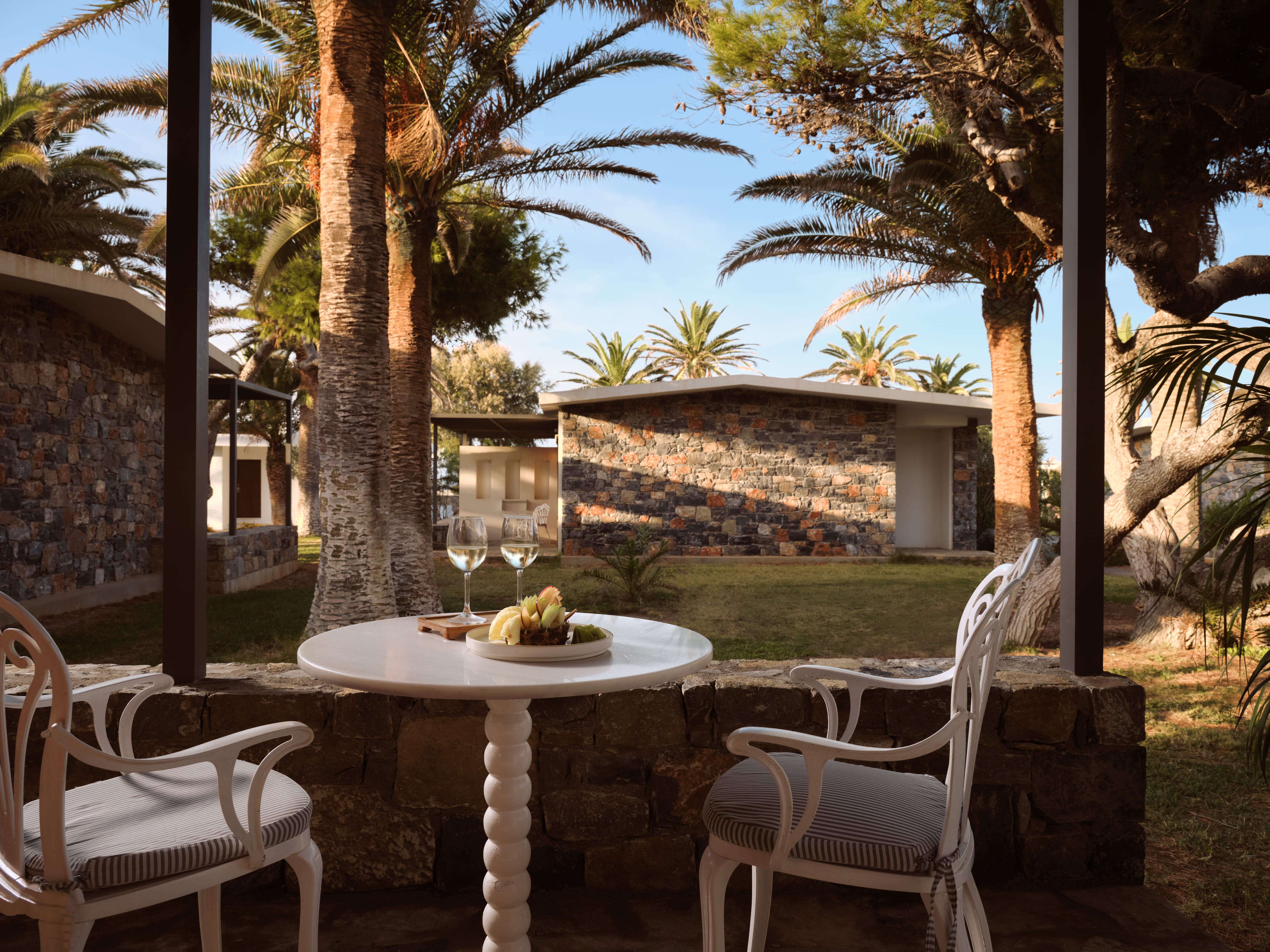 a table and chairs outside with a stone wall and trees
