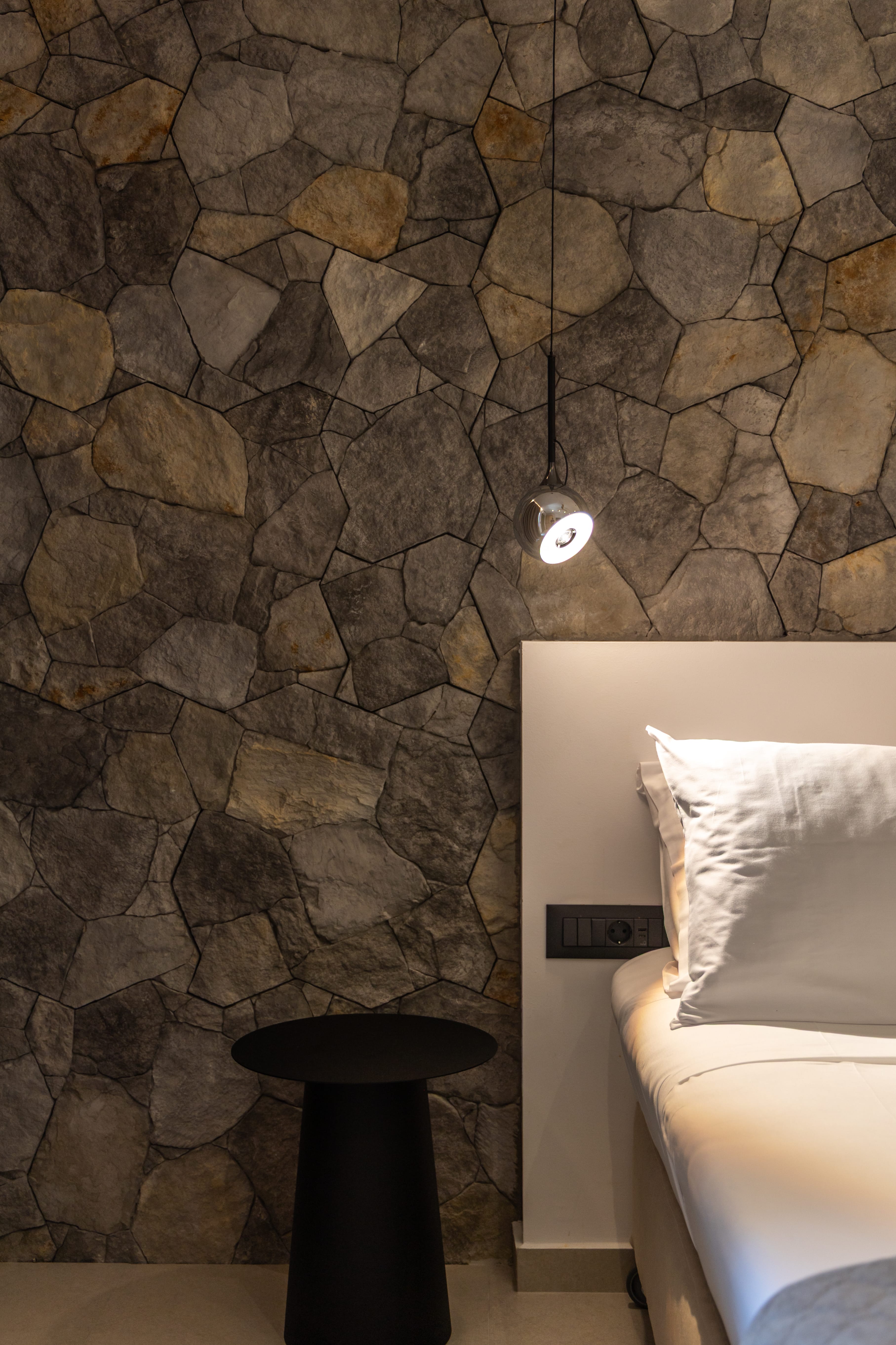 a bed with a lamp above a stone wall