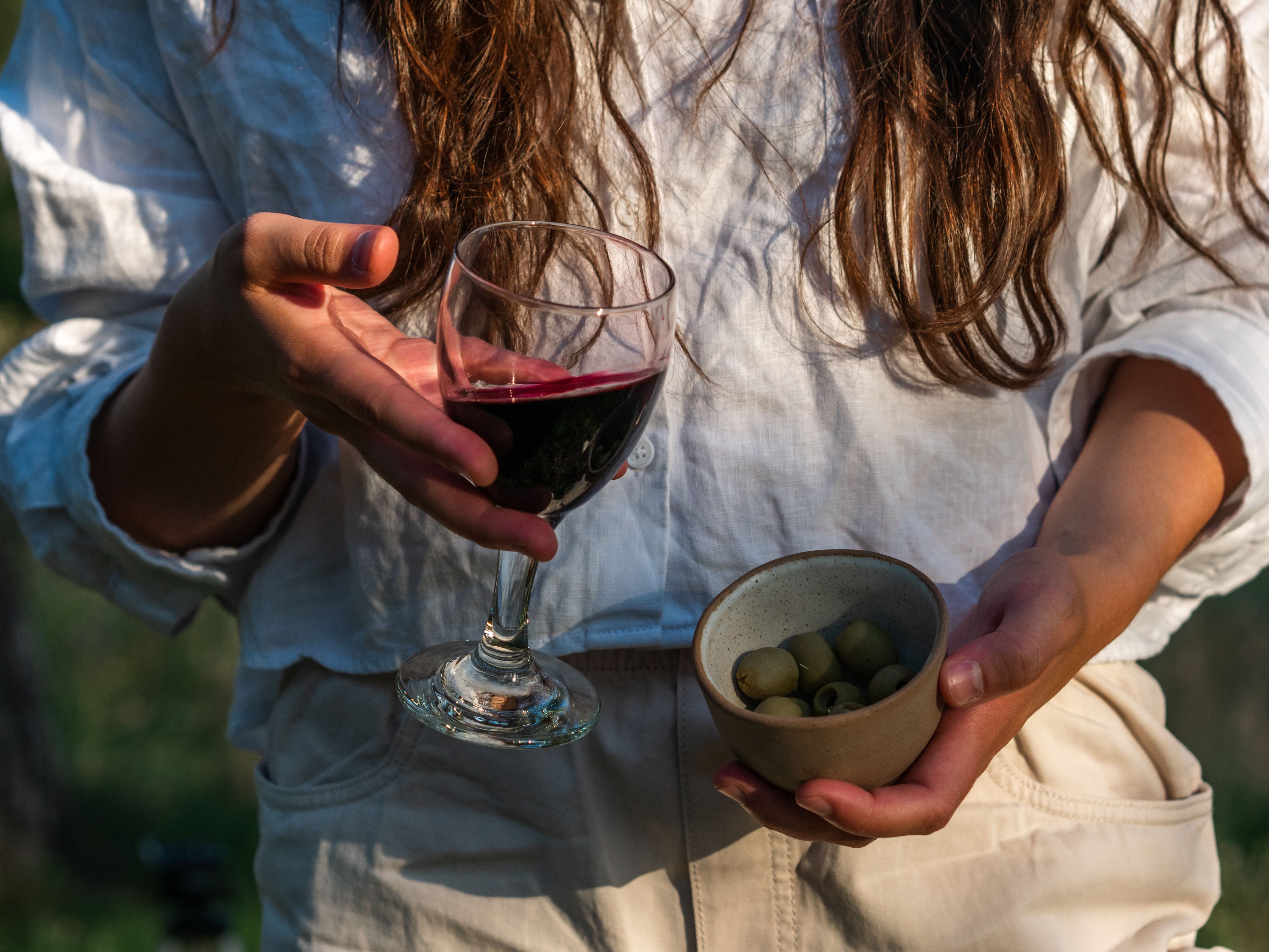 a person holding a glass of wine and a bowl of olives