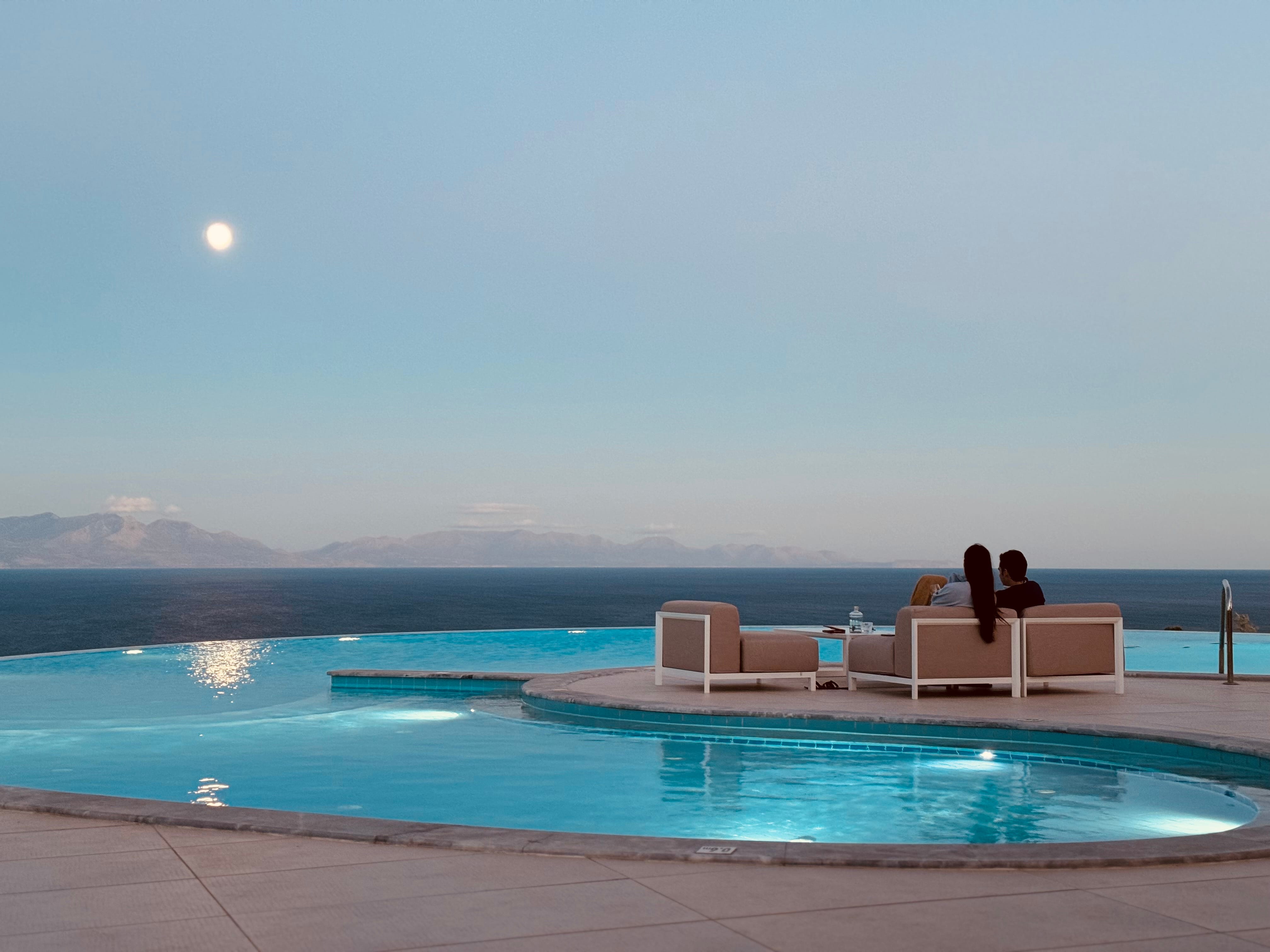 a pool with chairs and a person sitting on a bench by it