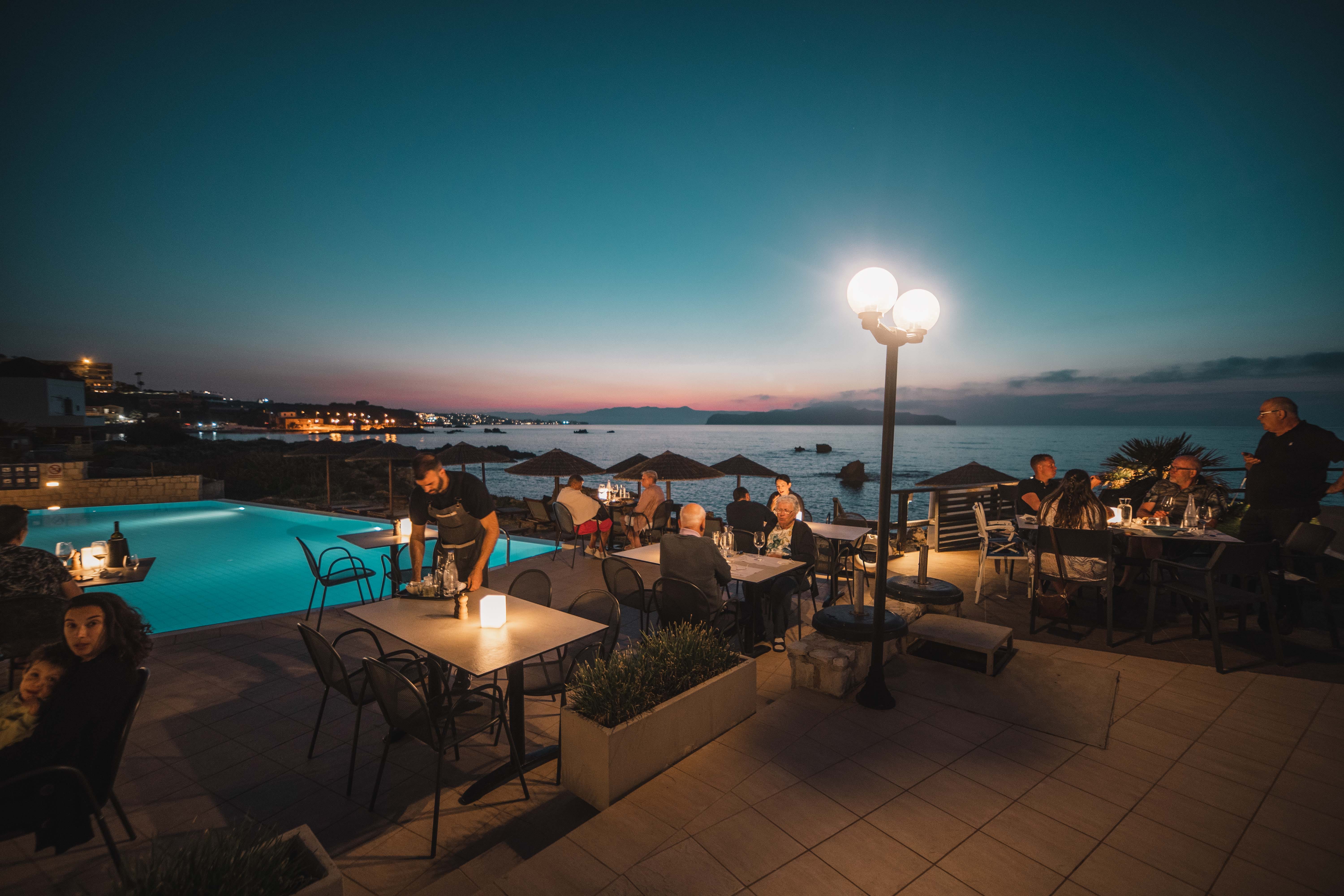 a group of people sitting at a table by a pool at night