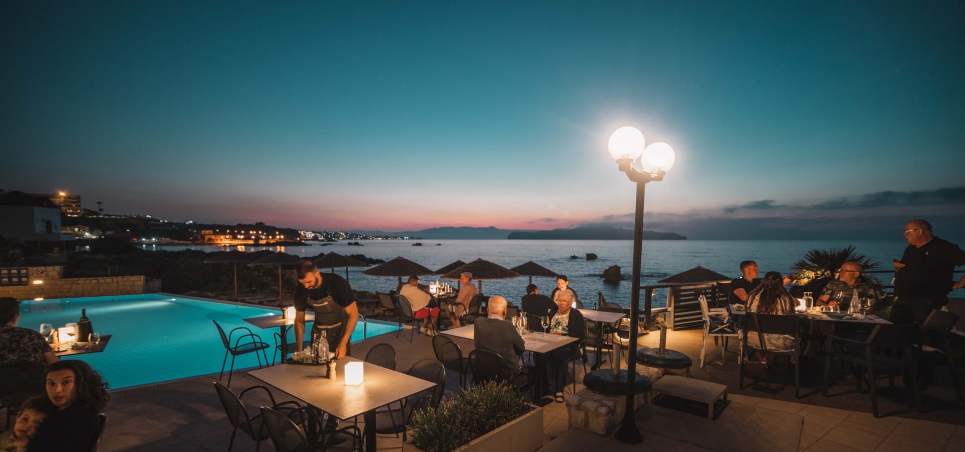 a group of people sitting at a table by a pool at night