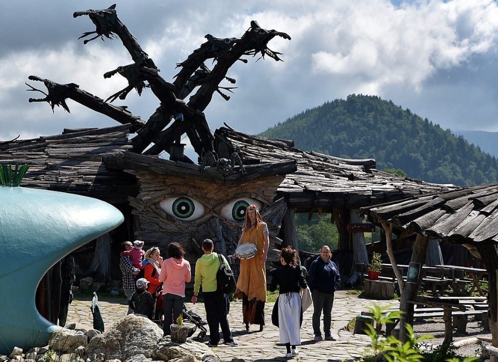 a dinosaur statue in front of a building with people walking around