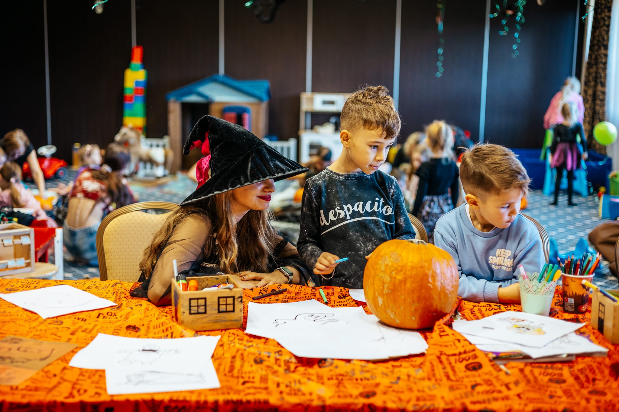 a group of kids sitting at a table with paper and a pumpkin