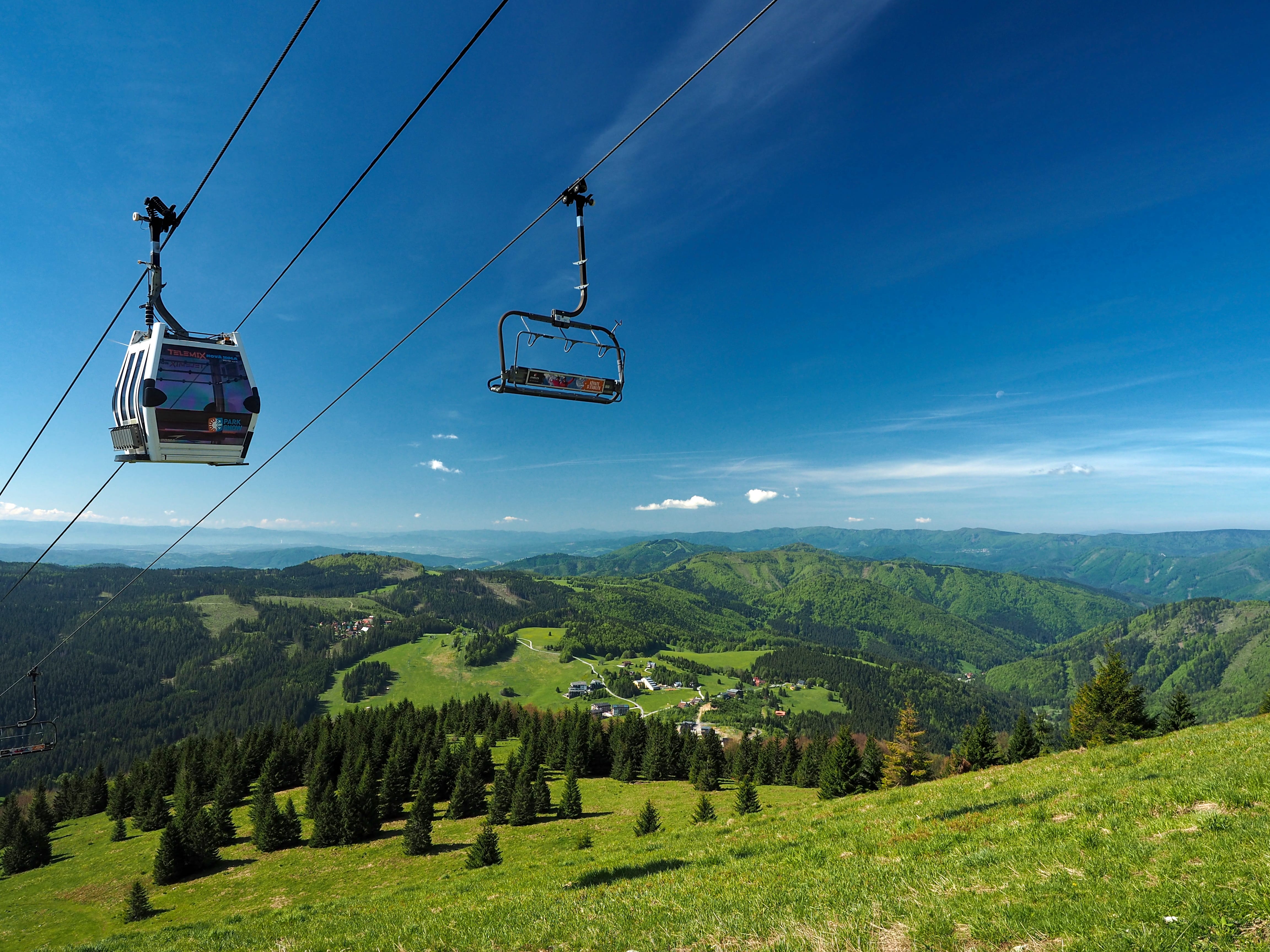a couple of chairs suspended above a grassy hill with trees and a blue sky