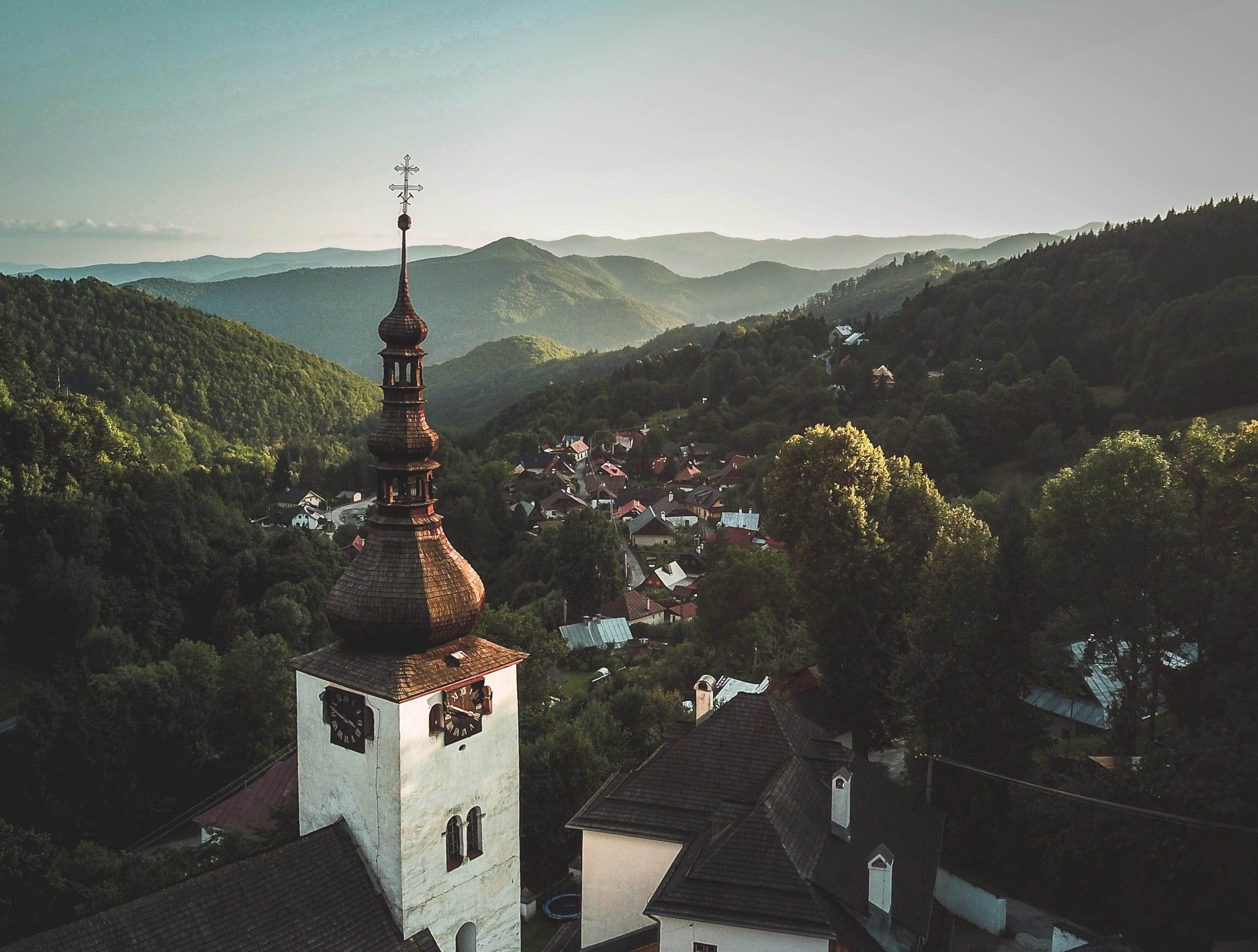 a tall tower with a cross on top surrounded by trees