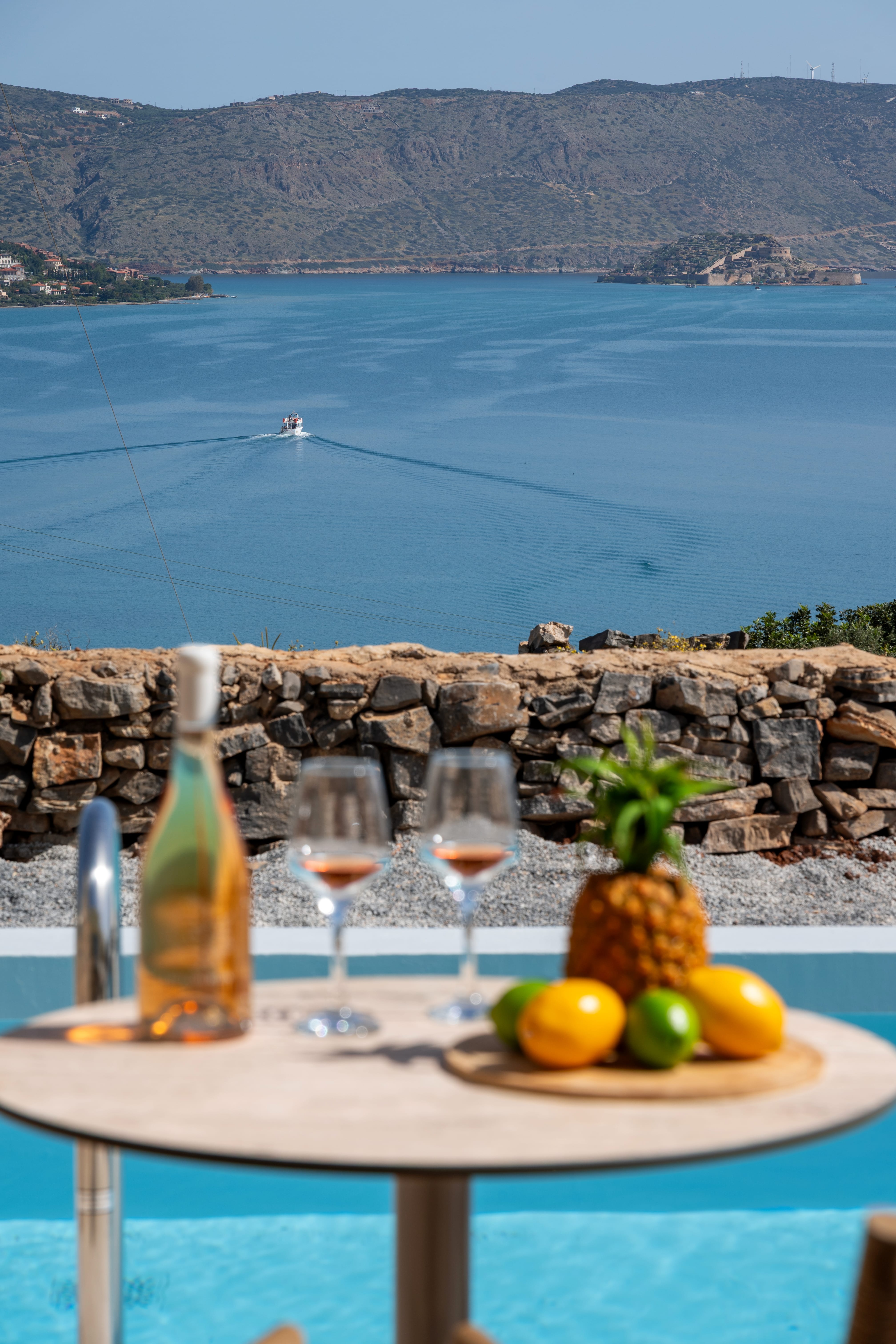 a table with fruit and wine glasses on it with a body of water in the background