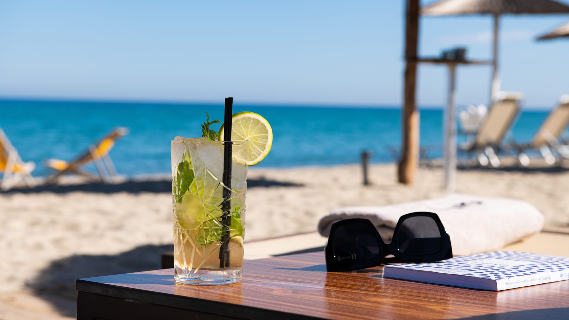 a glass with a drink on a table by a beach