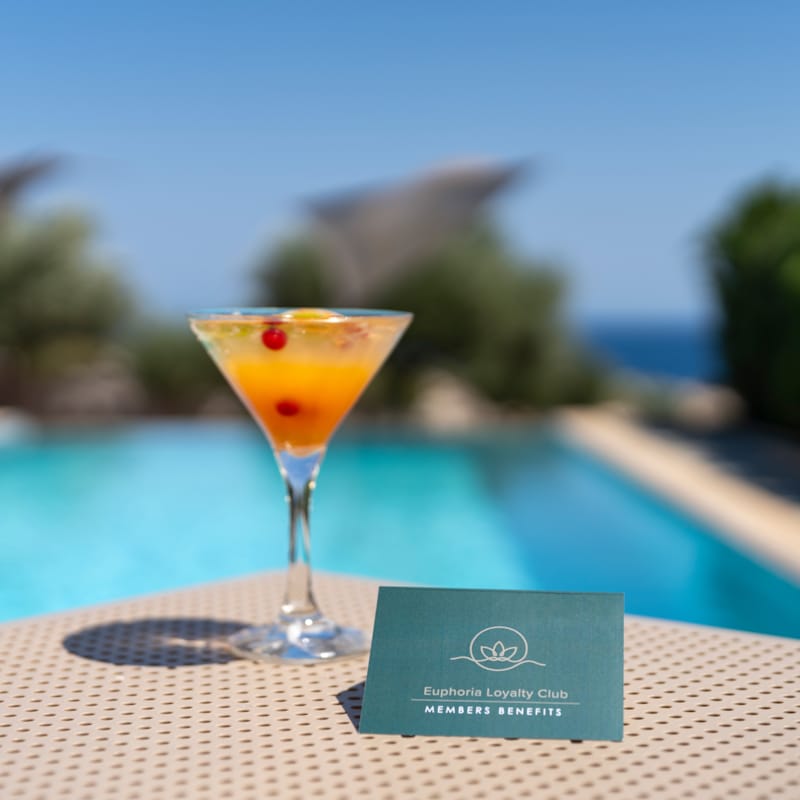 a glass of orange drink on a table by a pool