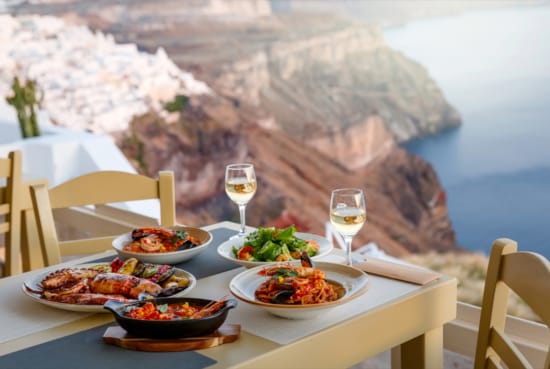 a table with food and glasses on it with a view of the ocean