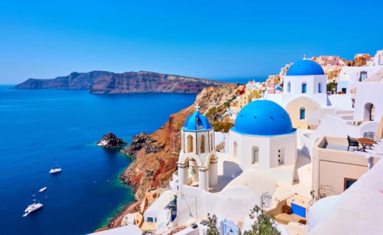 a white building on a cliff above water with Santorini in the background