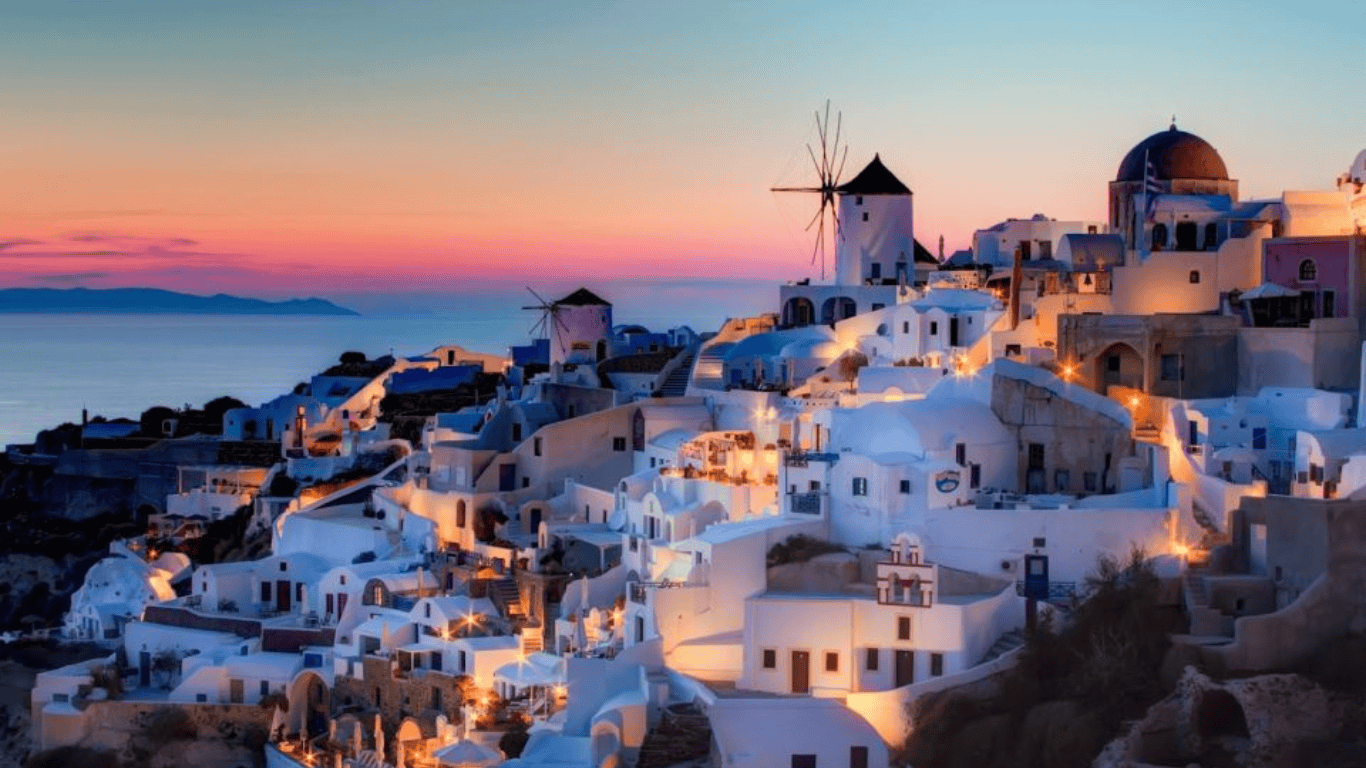 a town with white buildings and a body of water in the background with Santorini in the background