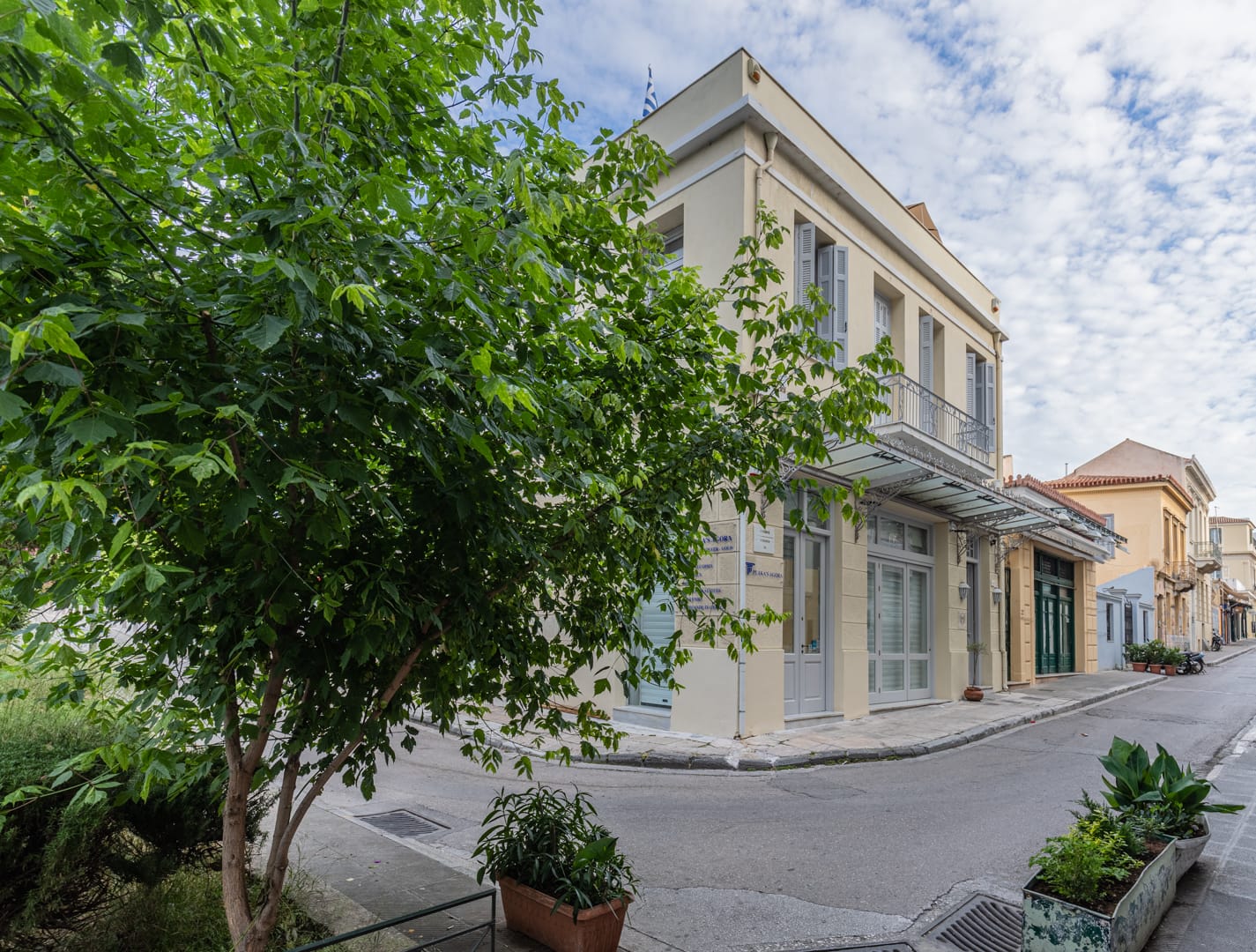 Exterior view of Kyria Boutique House with its elegant beige and white facade, located on a peaceful, tree-lined street in the historic Plaka district of Athens, showcasing traditional neighborhood architecture.