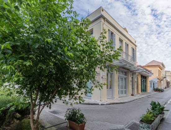 Exterior view of Kyria Boutique House with its elegant beige and white facade, located on a peaceful, tree-lined street in the historic Plaka district of Athens, showcasing traditional neighborhood architecture.