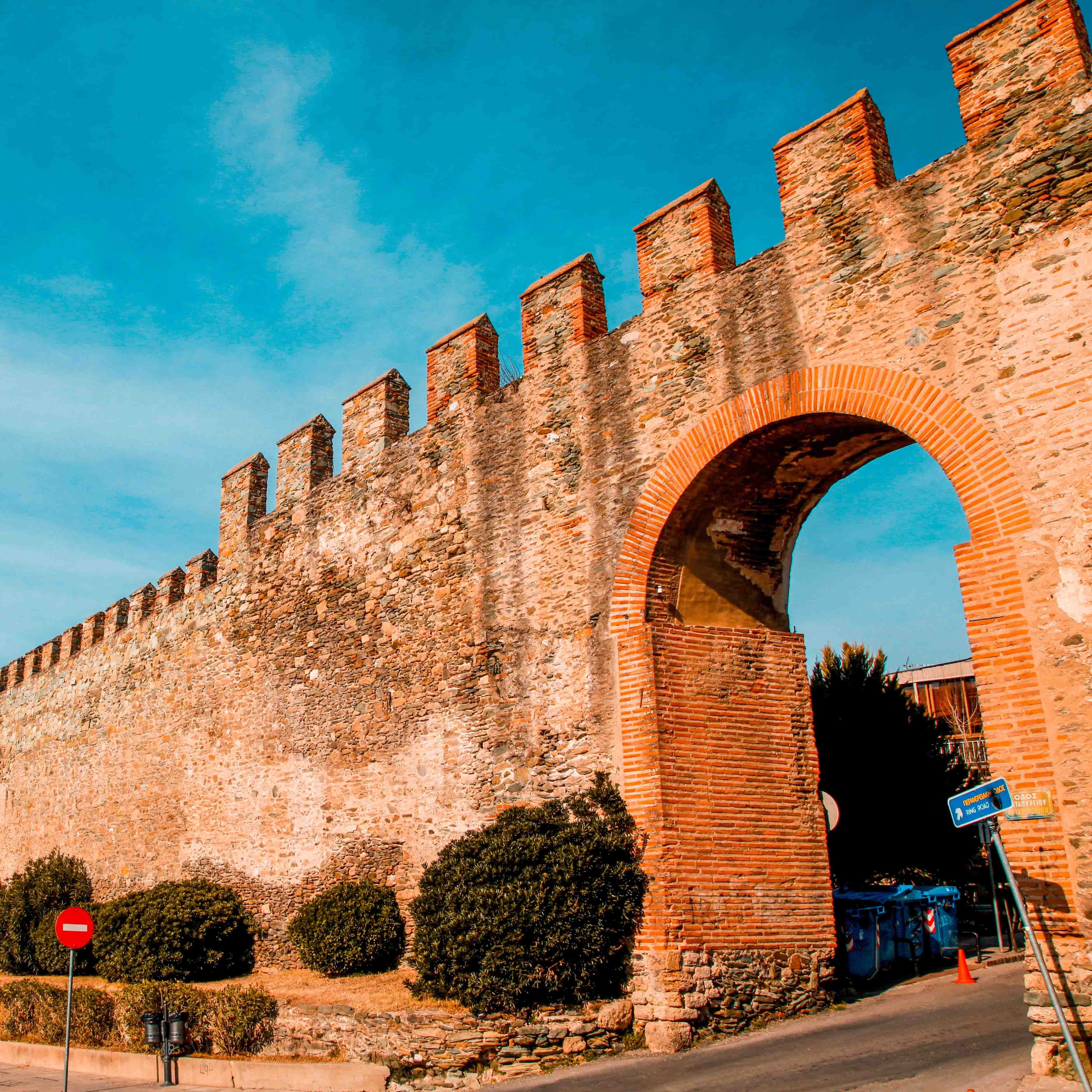 a brick archway with a road and bushes