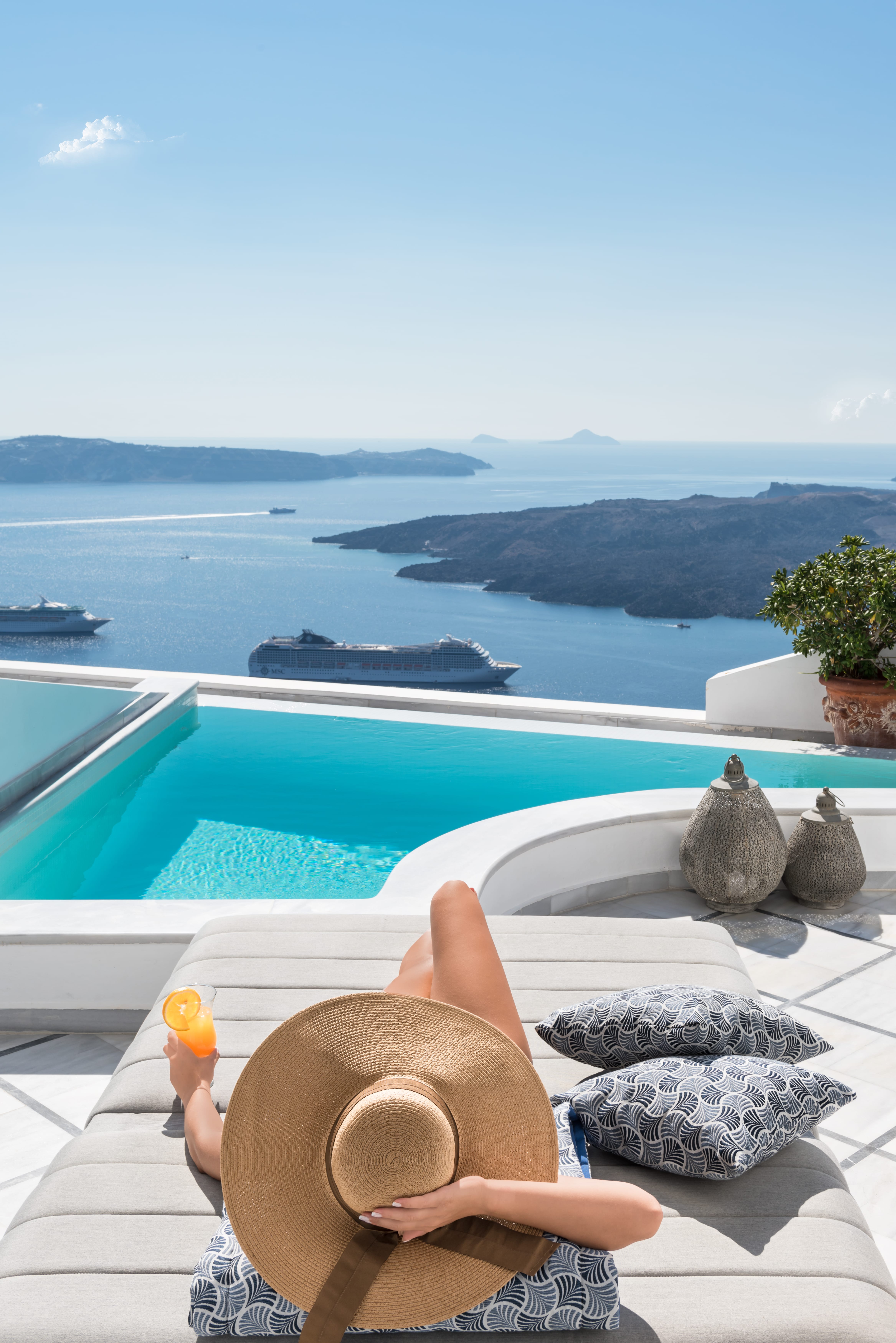 a hand holding a cup of coffee by a pool with a view of the ocean and islands