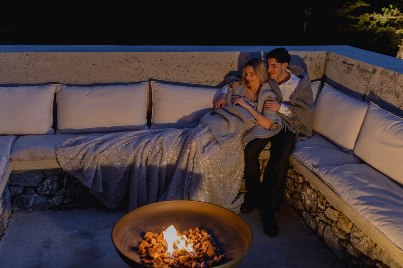 a man and woman sitting on a couch with a fire in front of them