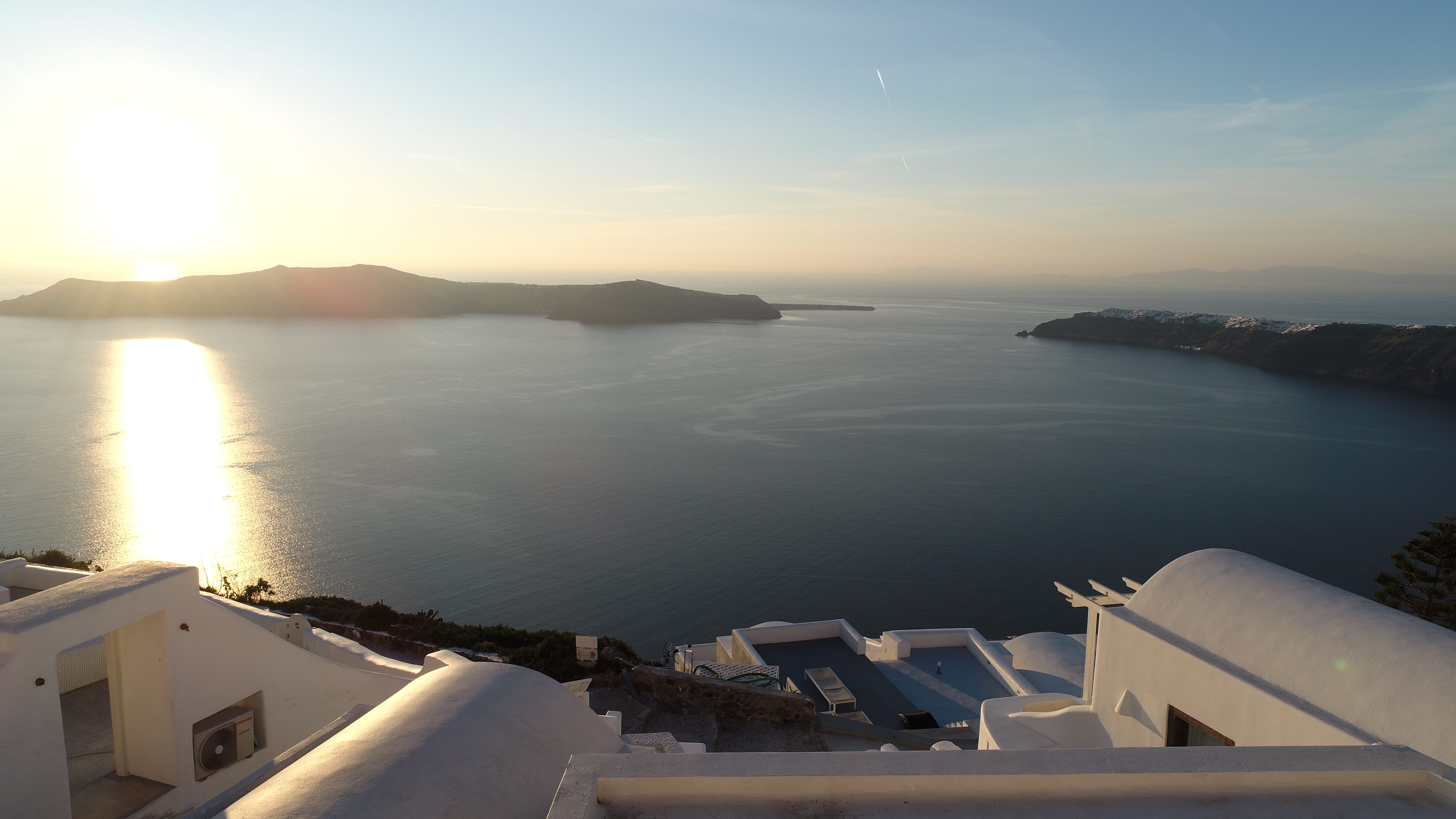a view of the ocean from a balcony with Santorini in the background