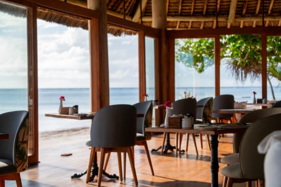 a room with tables and chairs and a body of water in the background
